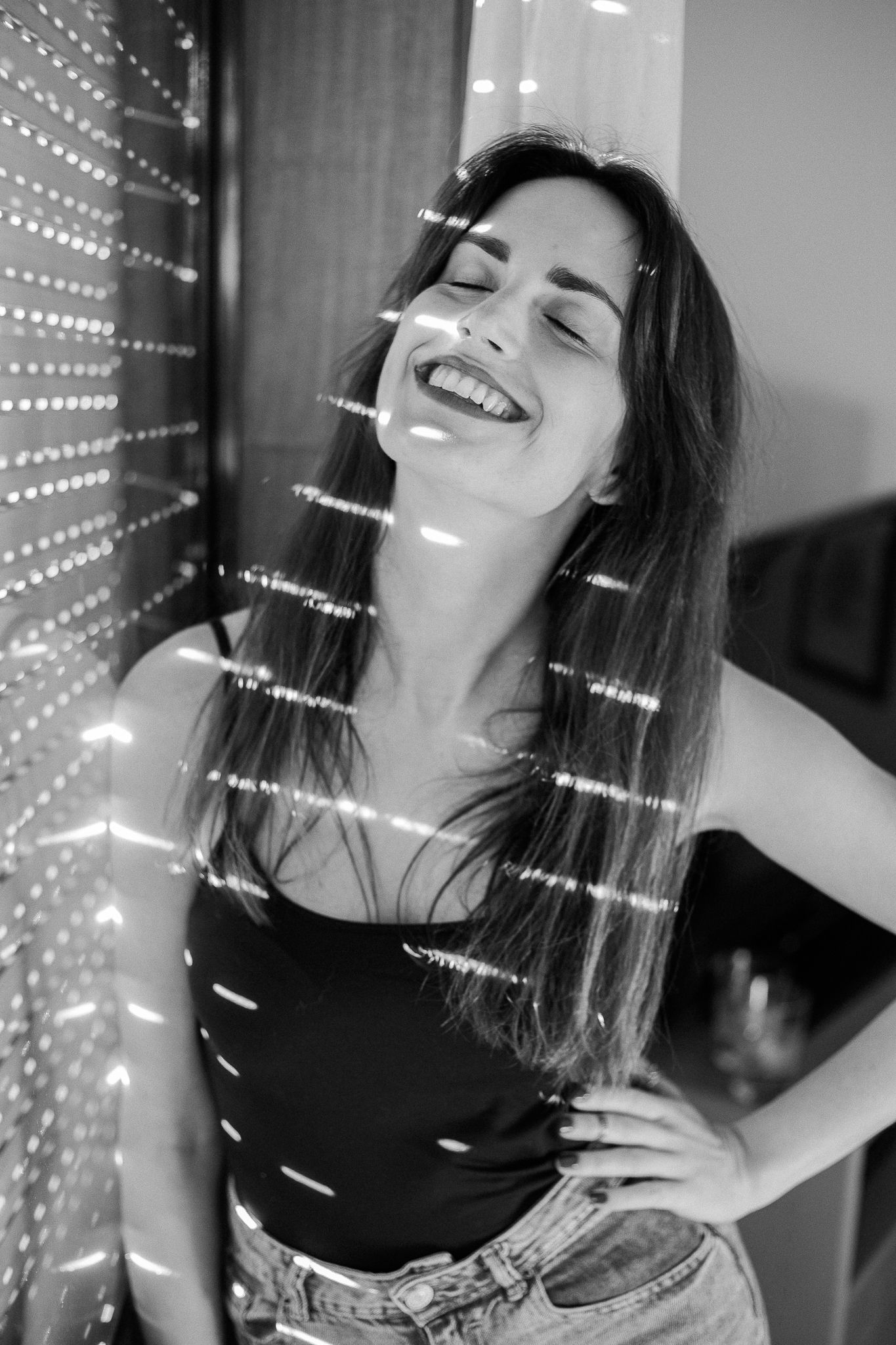 Joyful black and white portrait showing a woman laughing while standing near decorative string lights.