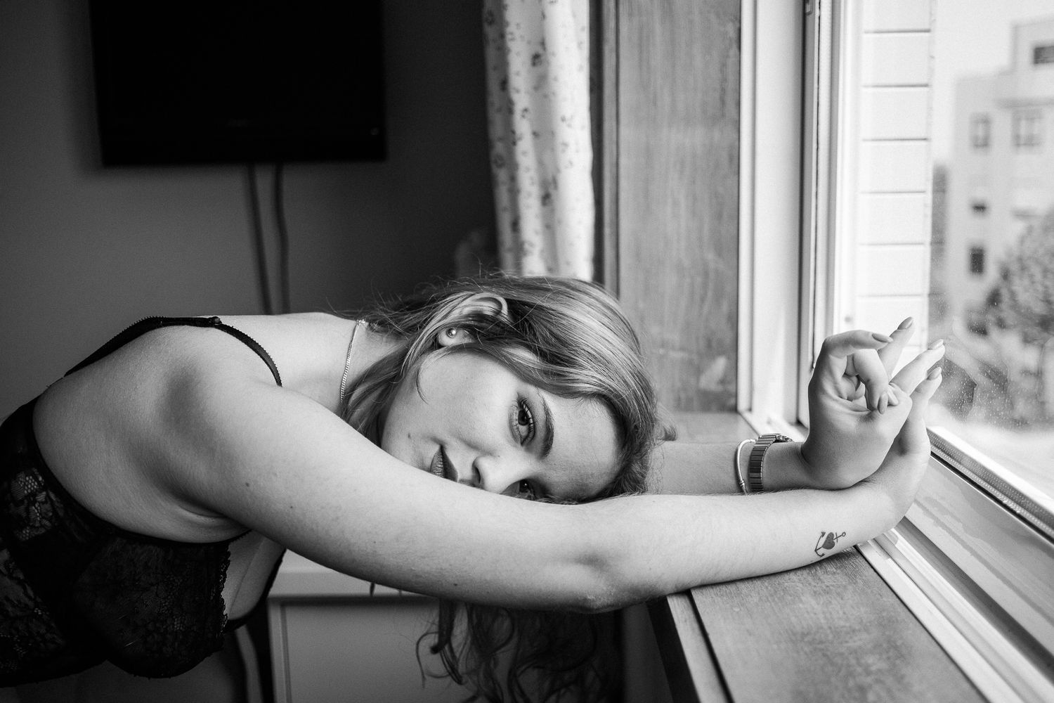 A person lies by a window sill in black and white, creating a moody and contemplative artistic portrait.