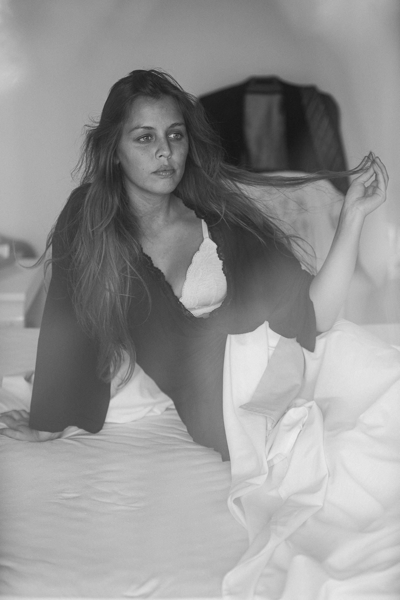 A black and white photo series showing someone lying on white bedding in various dramatic poses.