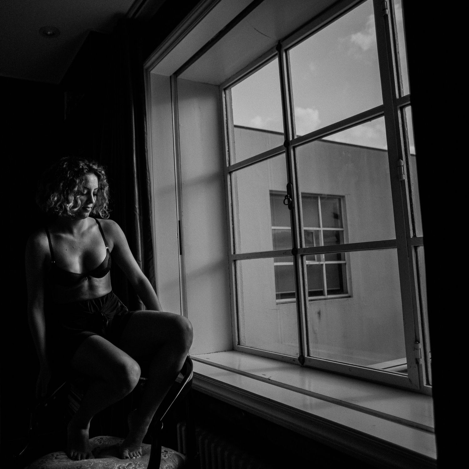 A black and white photo series showing a person looking out of a window in a contemplative, moody atmosphere.