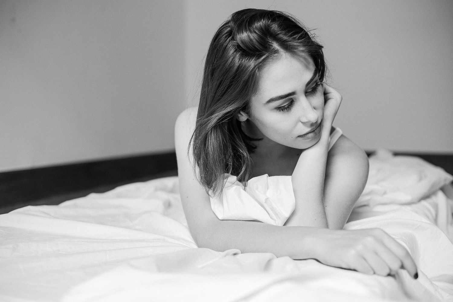 Black and white photo series showing a person lying on white bedding in various relaxed poses.
