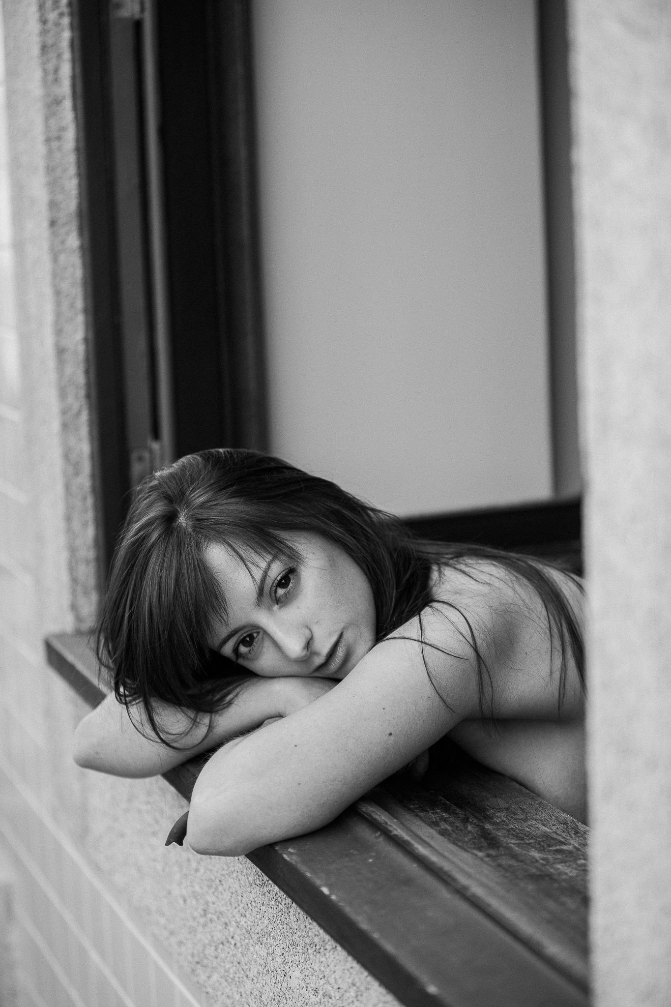 Moody black and white portrait of someone resting on a windowsill.