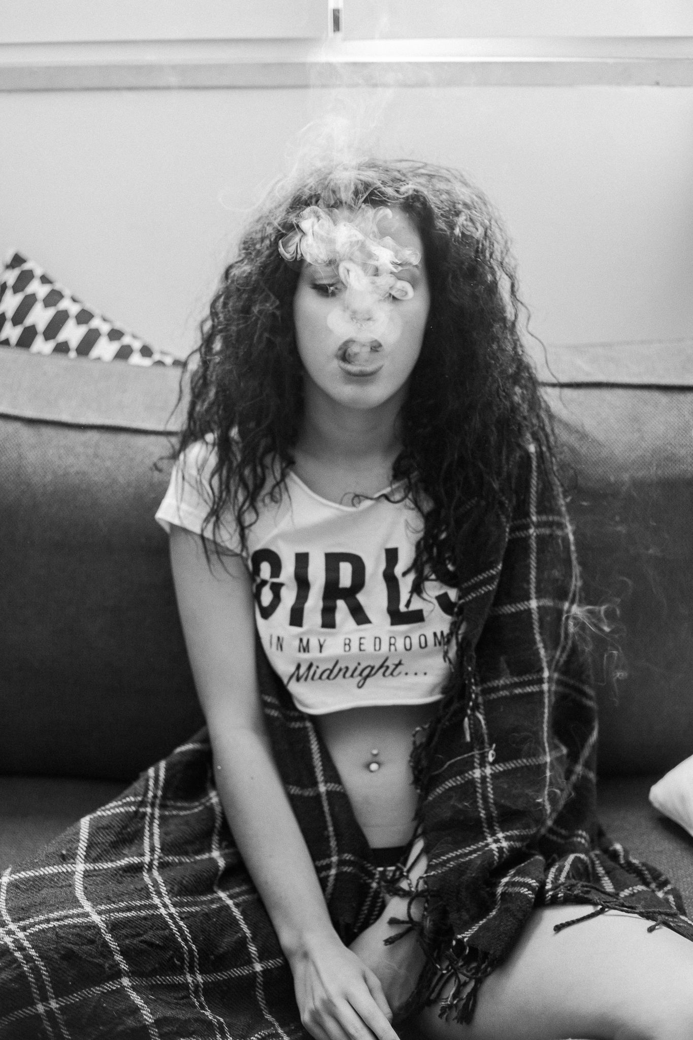 Black and white photo of someone in a cropped 'GIRL' t-shirt and plaid flannel sitting on a couch.