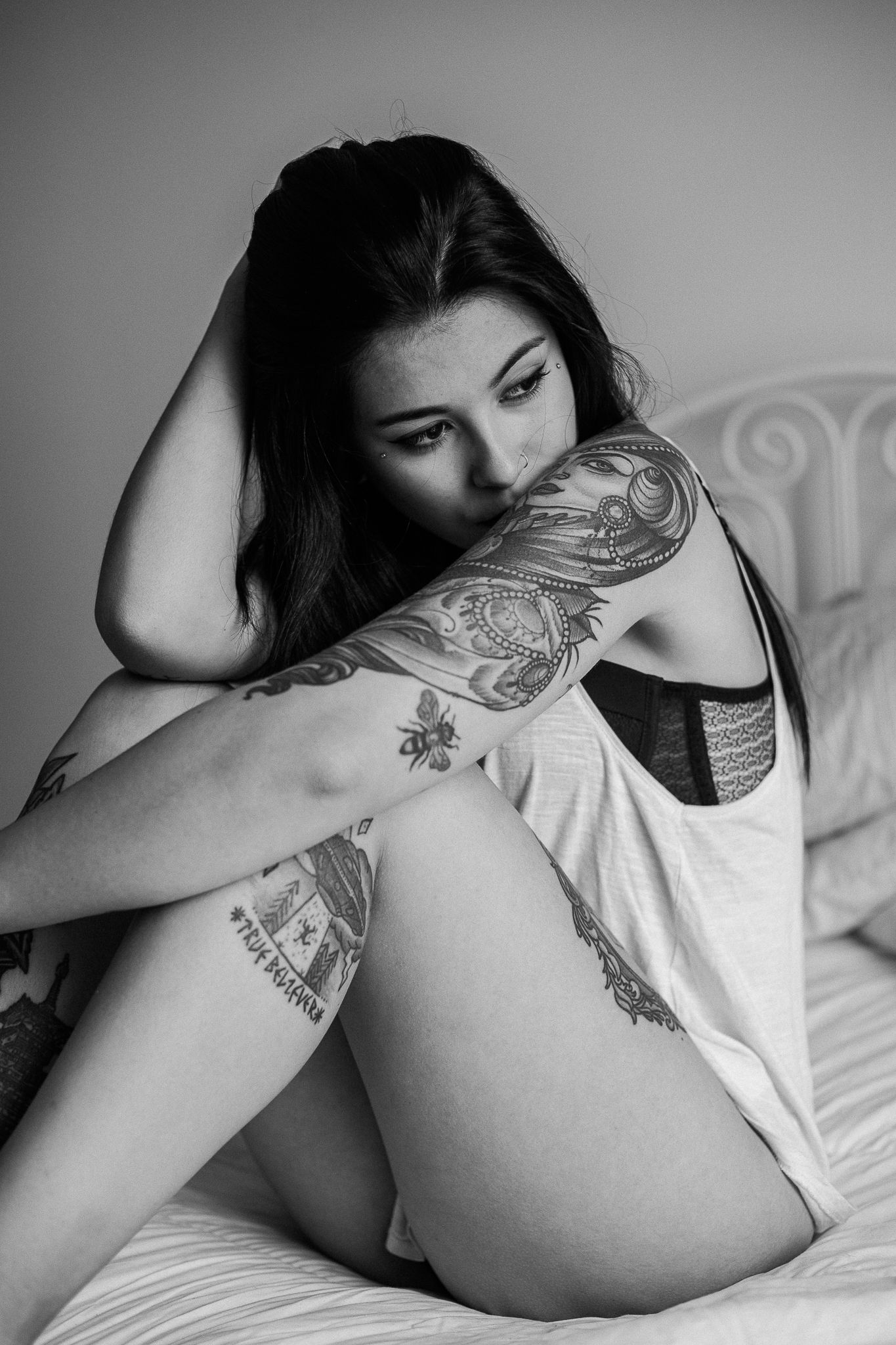 Black and white artistic boudoir photo sequence showing a reclining figure with tattoos on a white bed.