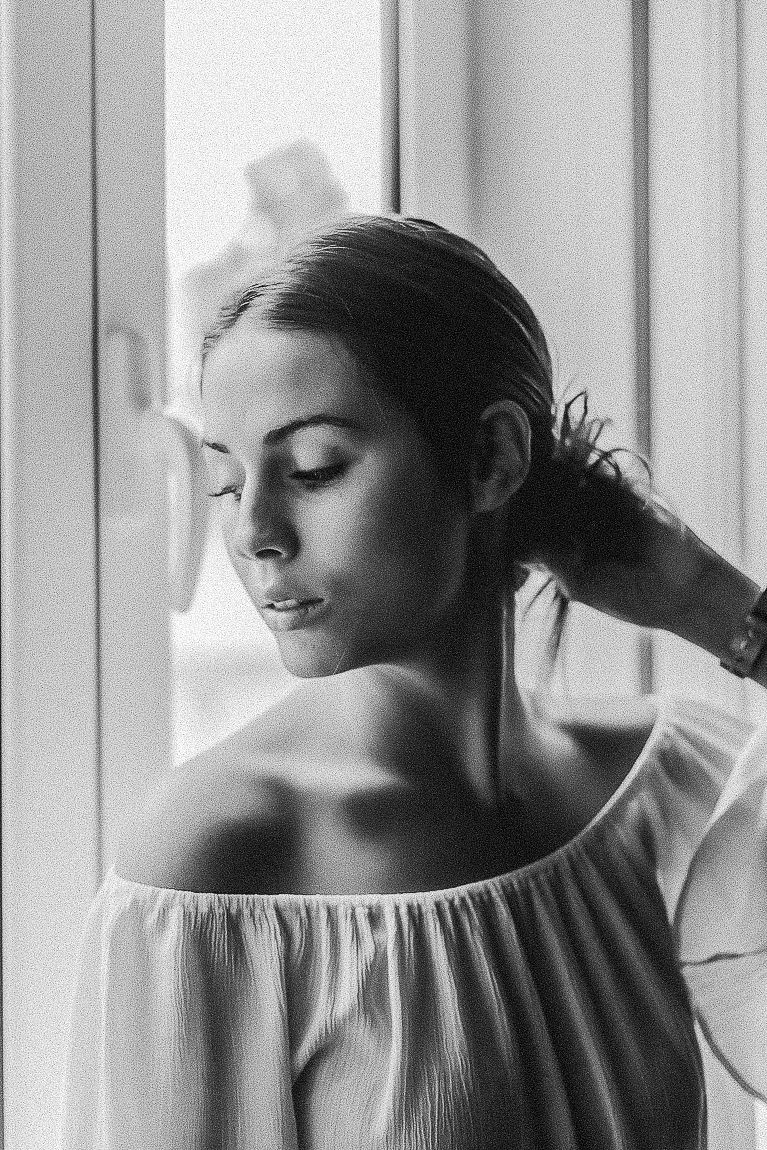 A series of black and white portraits showing a woman in an off-shoulder dress near a window in soft natural light.