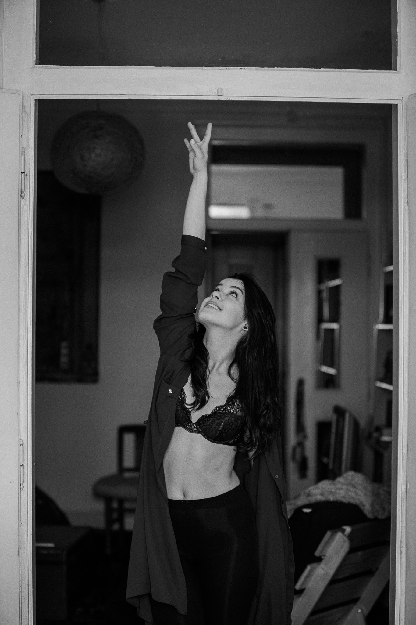 A person in black clothing dances expressively in front of white window frames in an indoor setting.