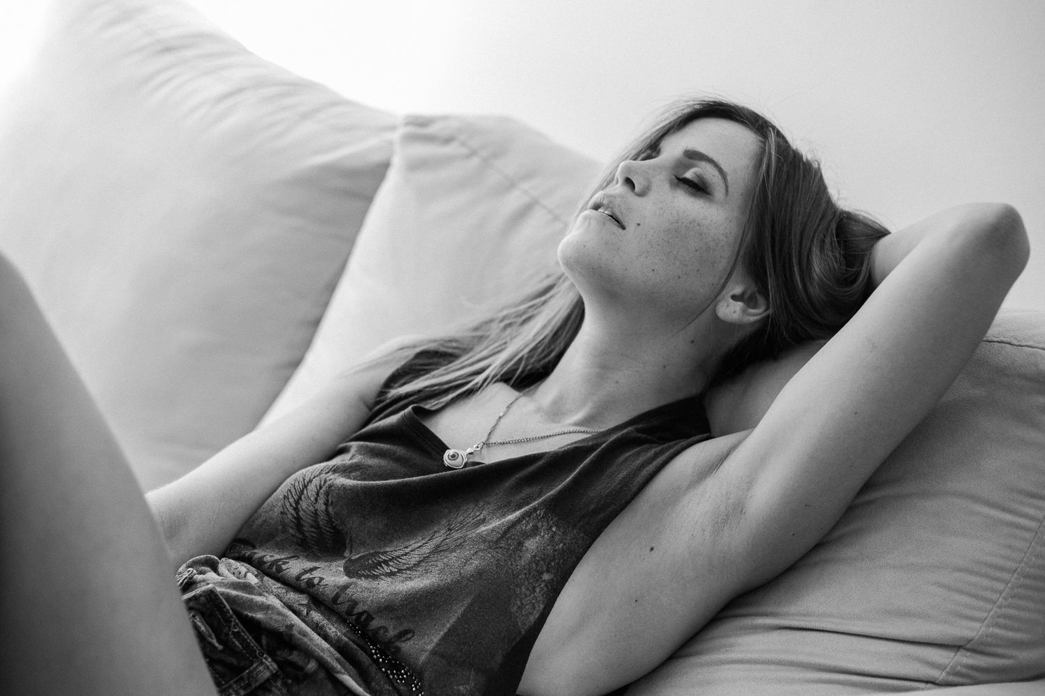 Person lying down on white bedding in a relaxed pose with arms raised.
