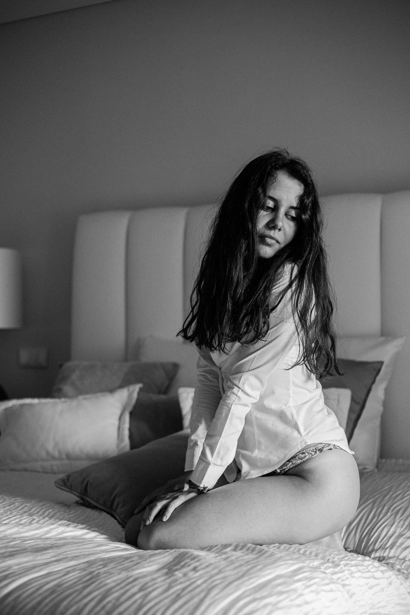 Dramatic bedroom photoshoot showing poses on white bedding in monochrome.