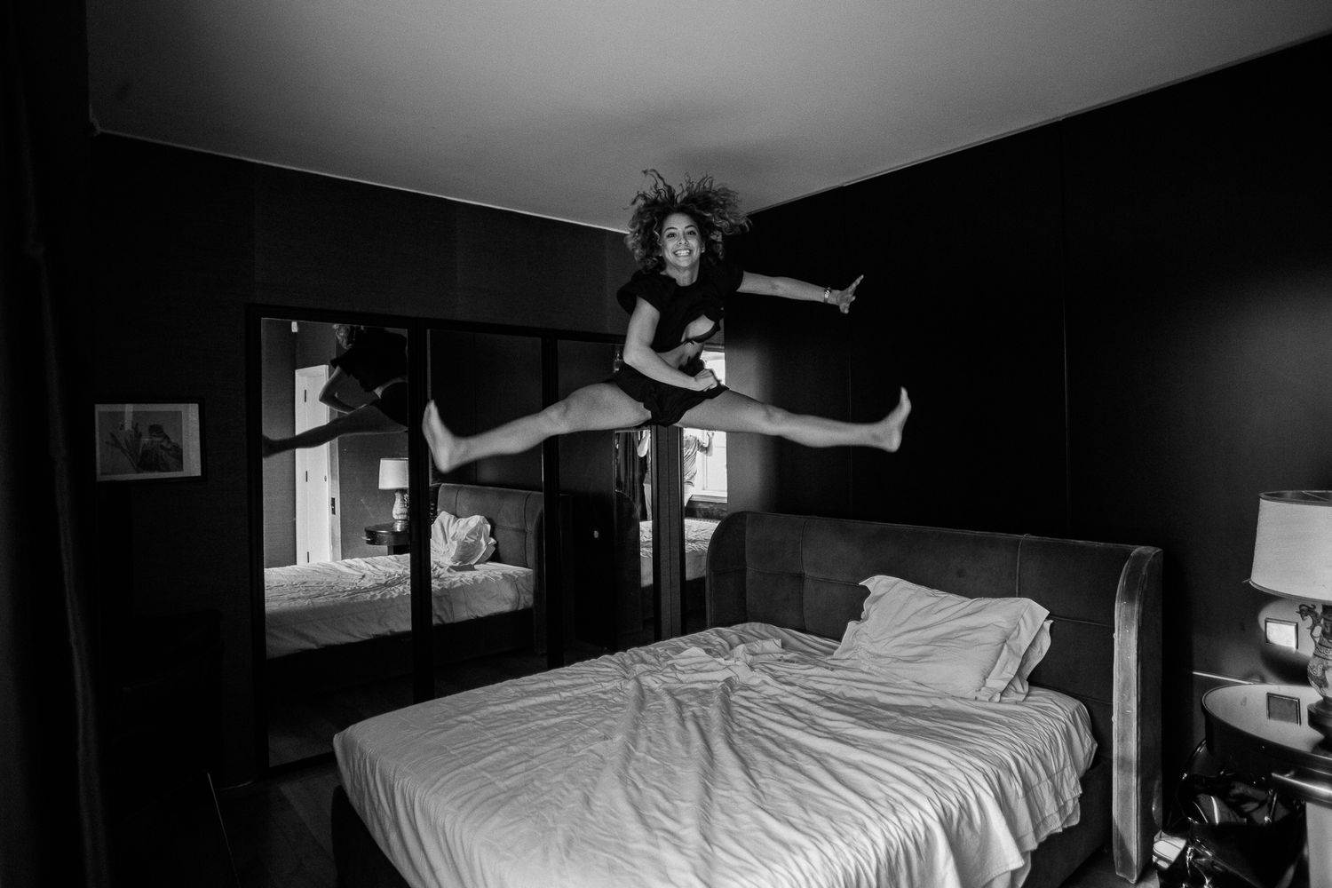 Dynamic black and white photo of a person jumping on a bed in a dark room.