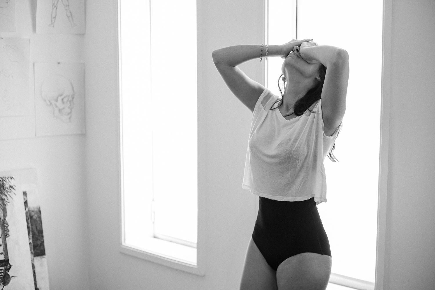 A black and white photo series showing someone posing and stretching in various positions against a white wall.