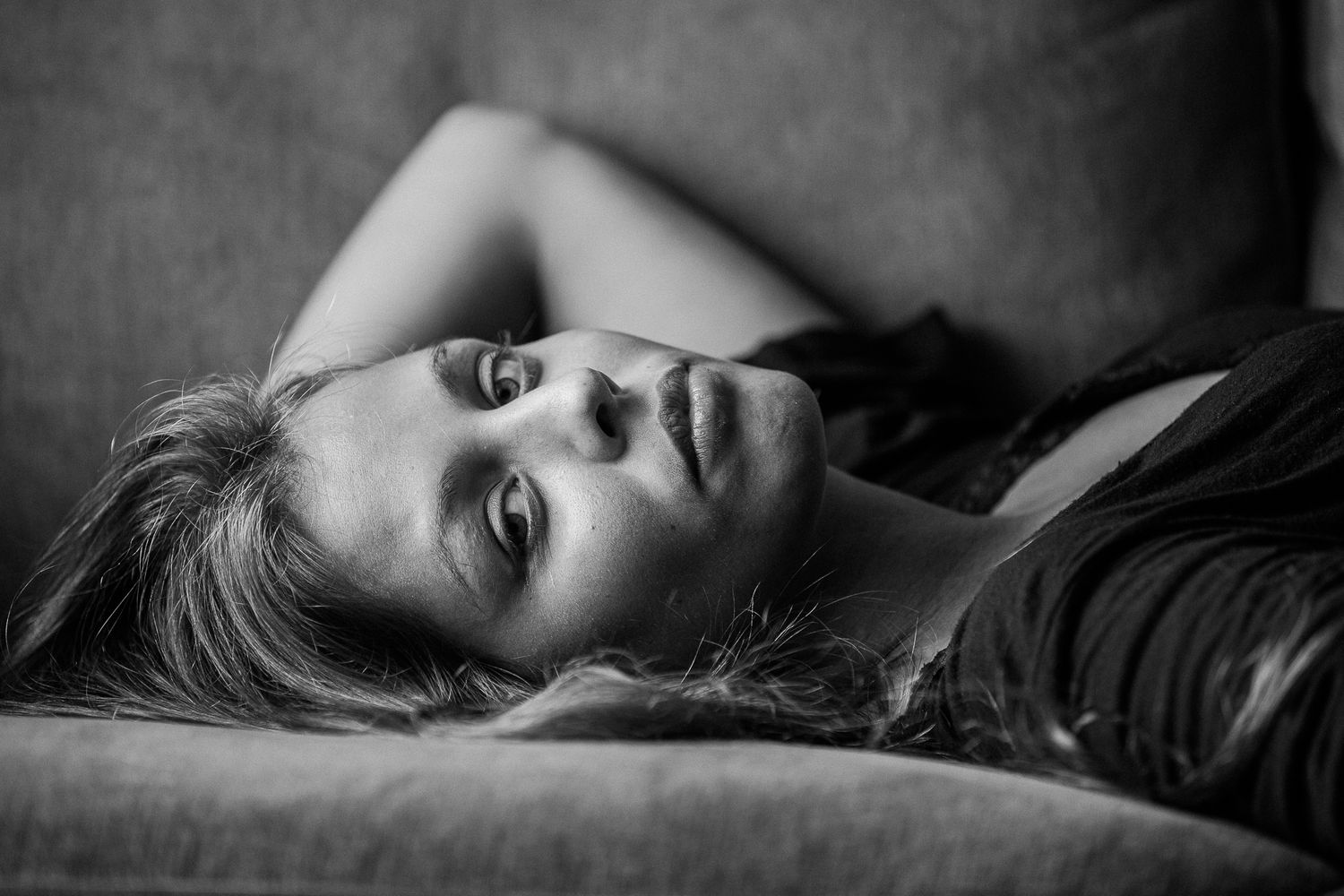 Artistic black and white headshot of woman with dark hair lying down in dramatic lighting.