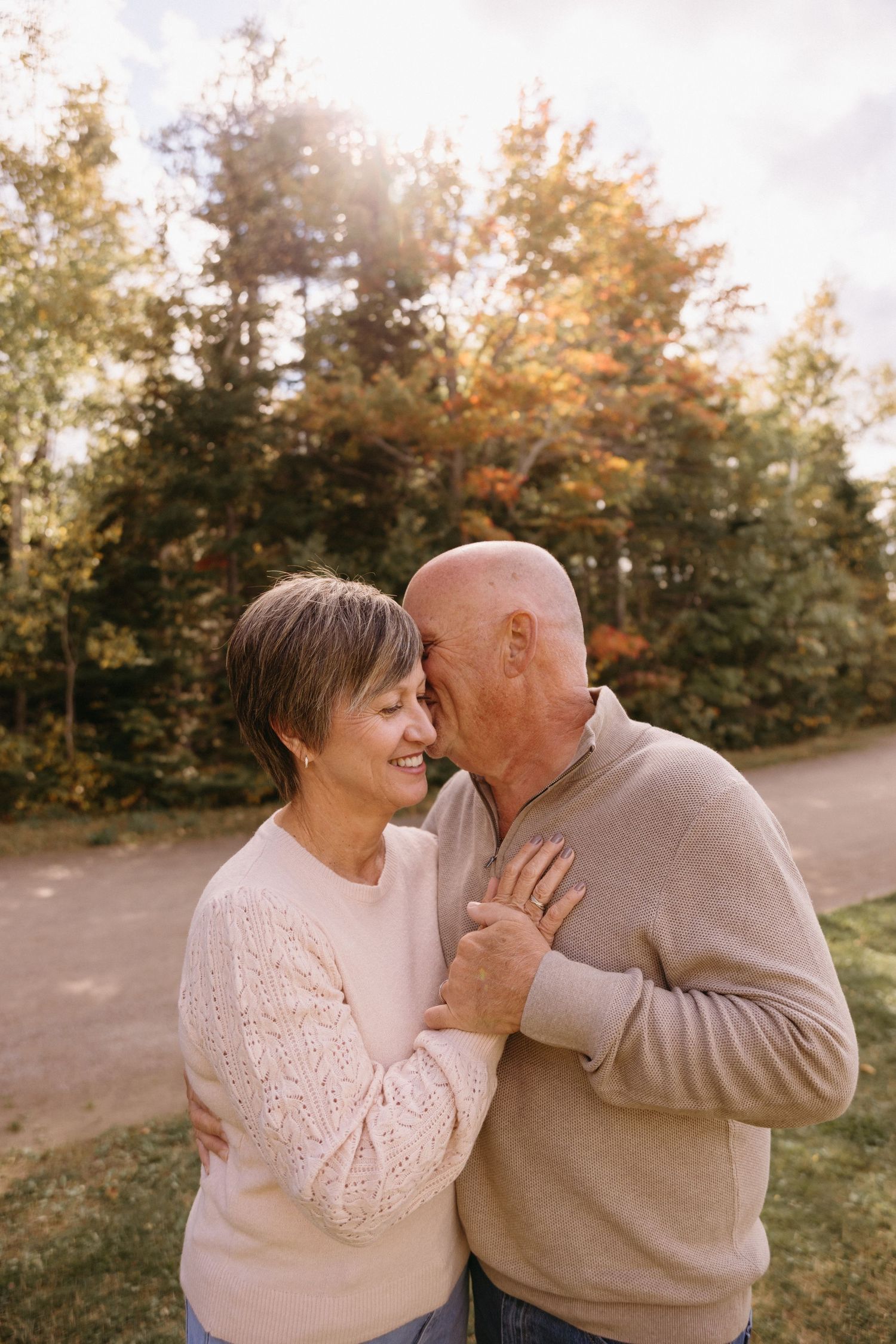A couple shares loving glances and laughter in a sunlit outdoor setting with fall foliage.