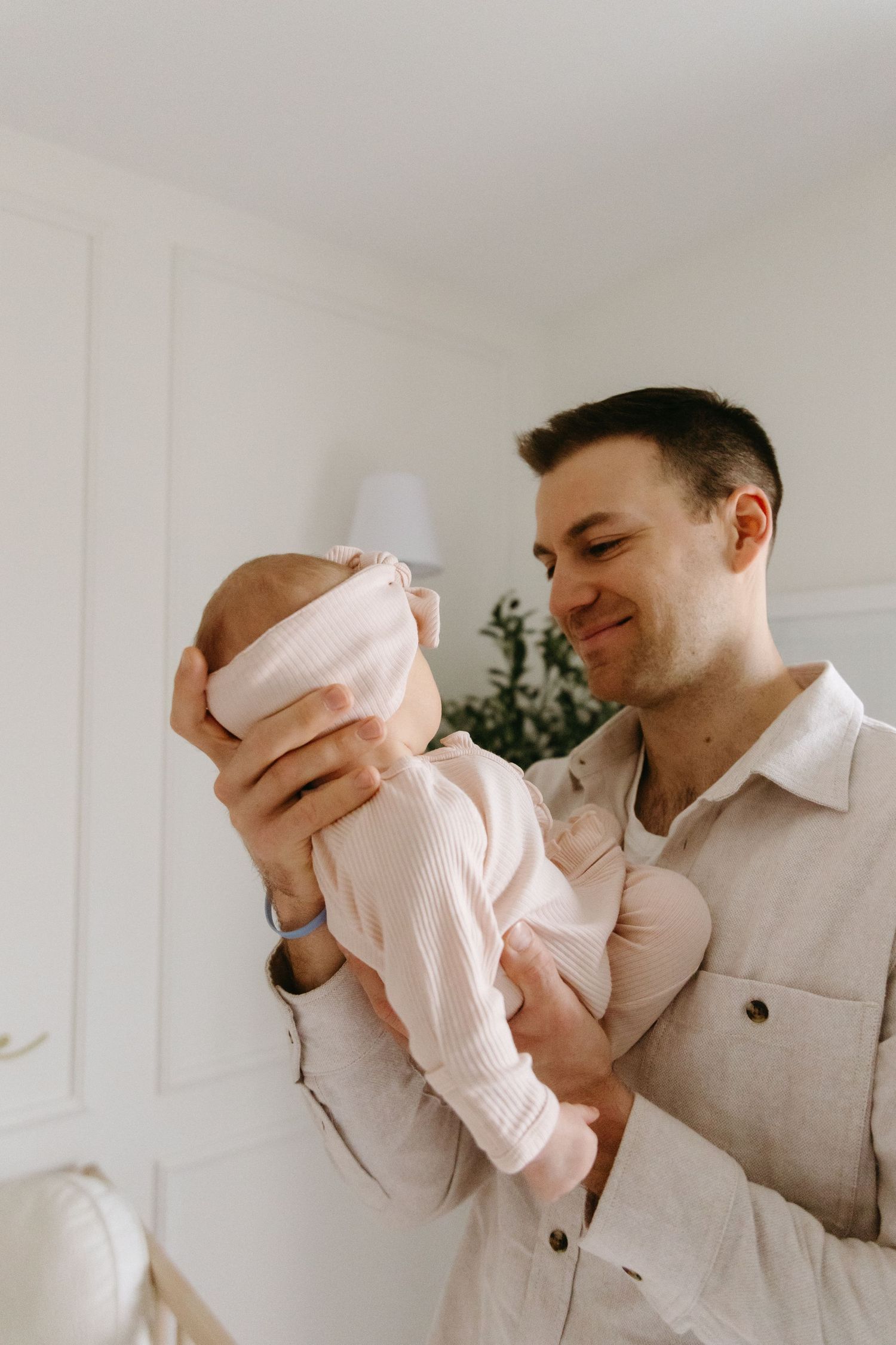 A parent in a light colored shirt holds and lovingly gazes at their newborn baby in a bright, minimalist setting.