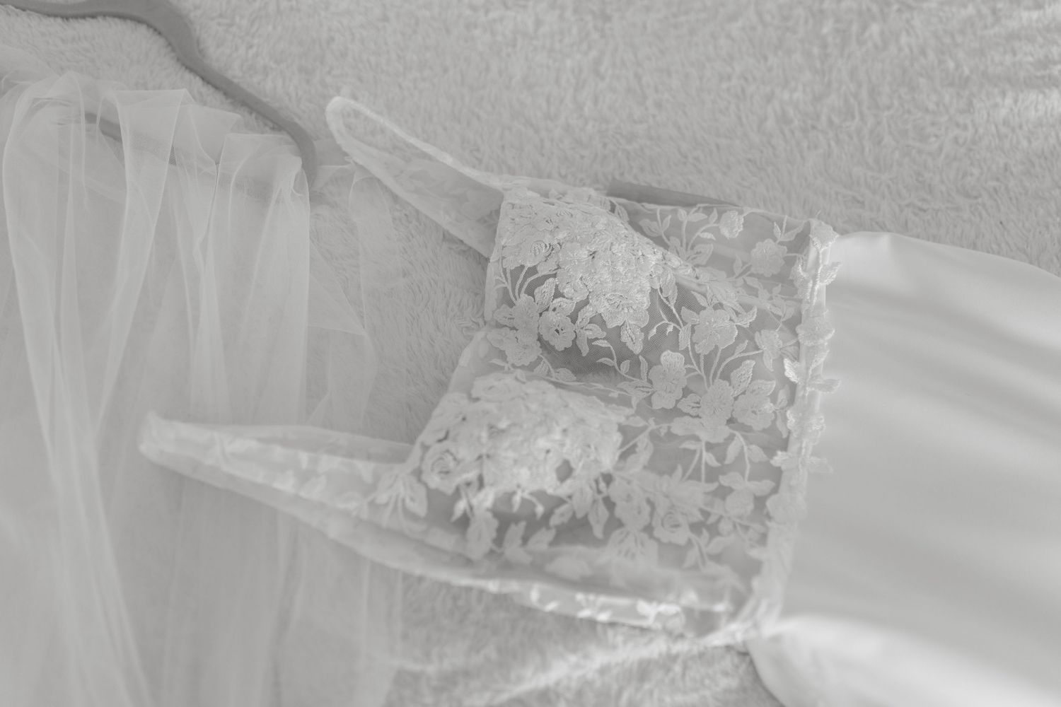 Detailed lace pattern on white wedding dress fabric with soft tulle overlay.