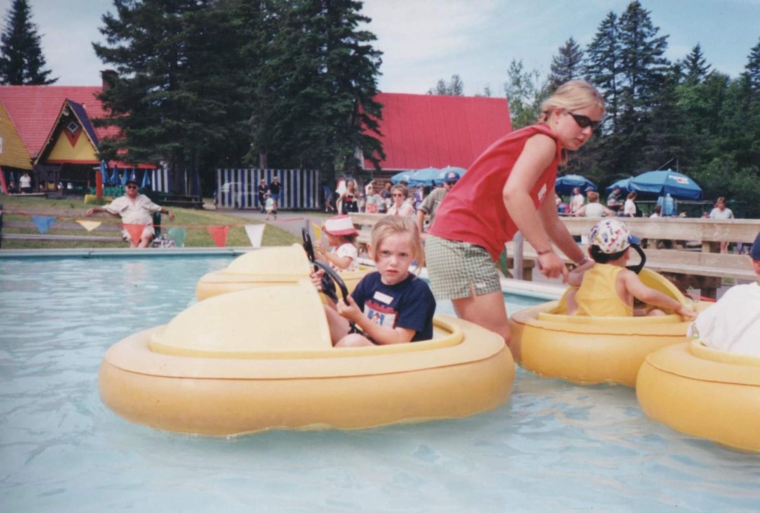People enjoying summer fun on yellow inner tubes floating in a lake surrounded by pine trees.