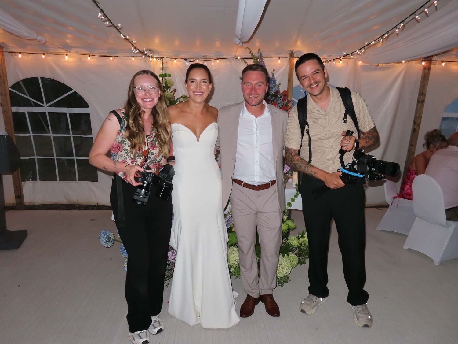 People dancing and celebrating at a wedding reception in a white tent with string lights overhead.