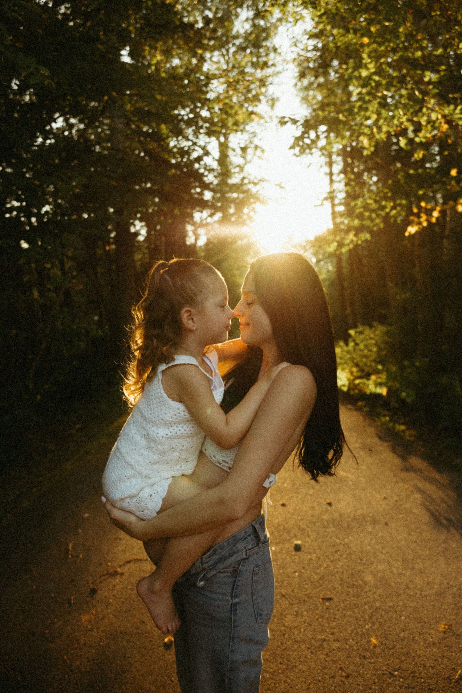 A tender moment between two people sharing a kiss on a sunlit forest path during golden hour.