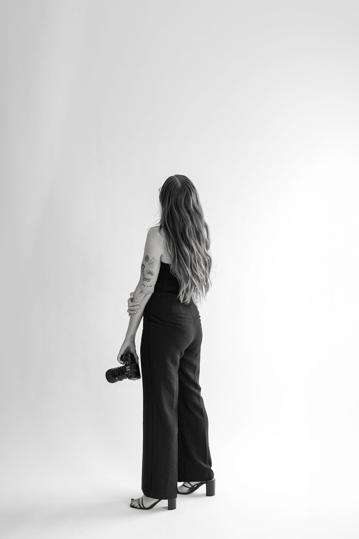 Back view of someone with long hair holding a camera while wearing business attire.