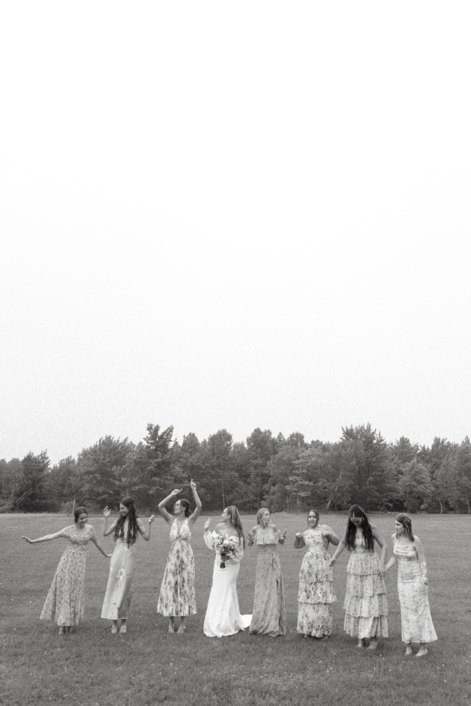 Group of people in light dresses standing in a line across a grassy field.