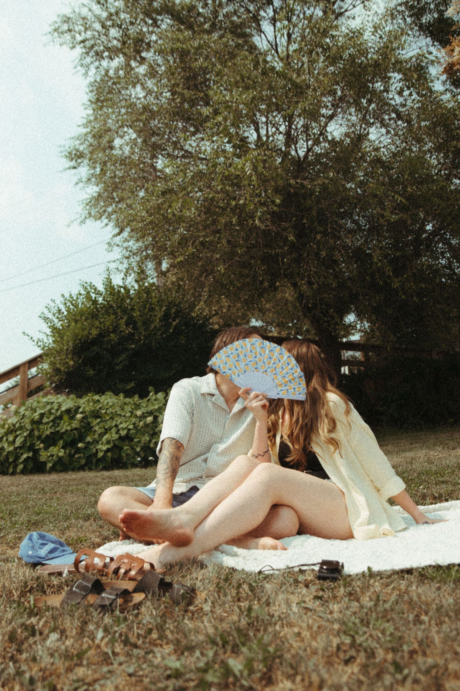 A person in a white dress lies on a blanket in a grassy field reading a book on a sunny afternoon.