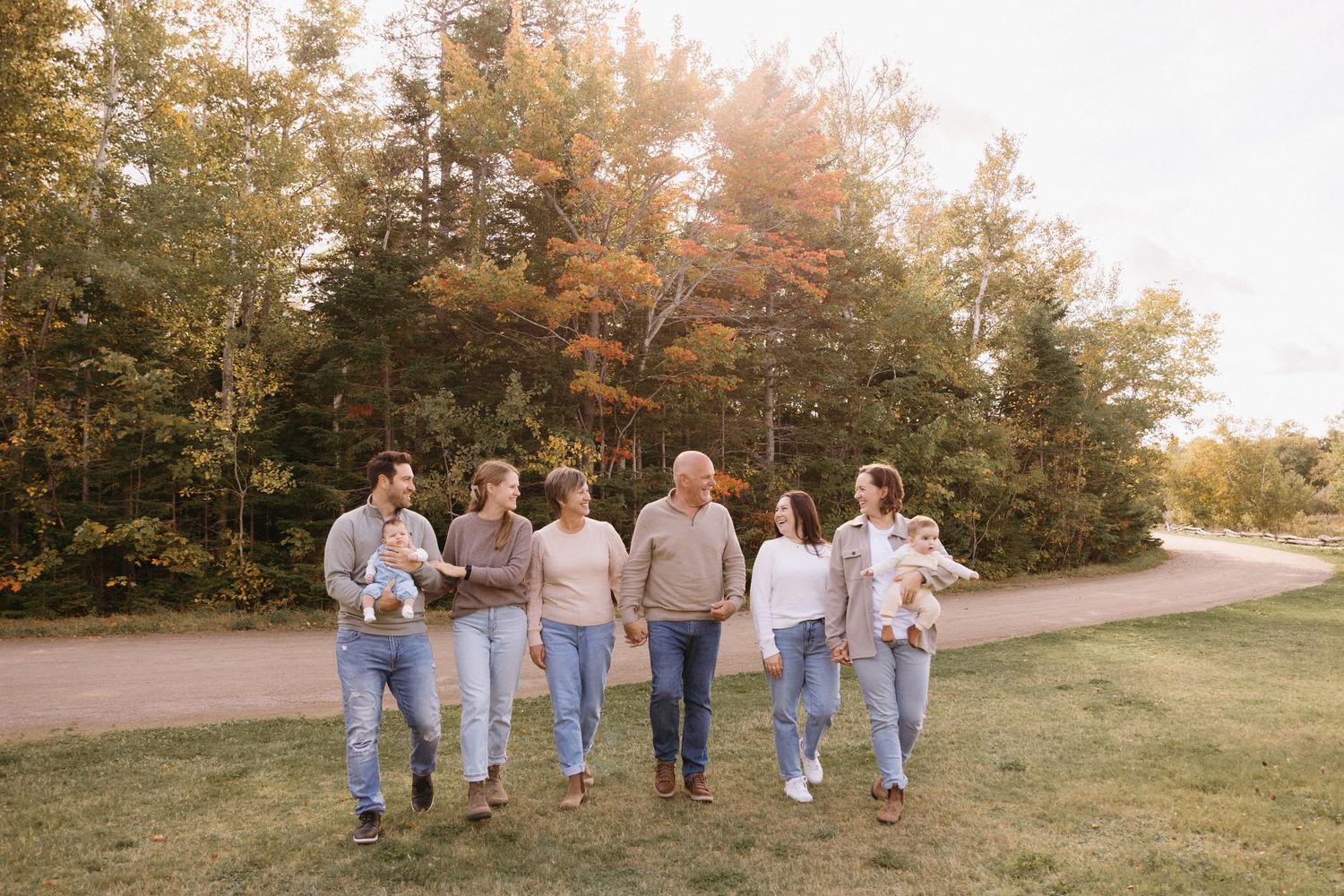 Family members stroll through a scenic outdoor setting with fall foliage in the background.