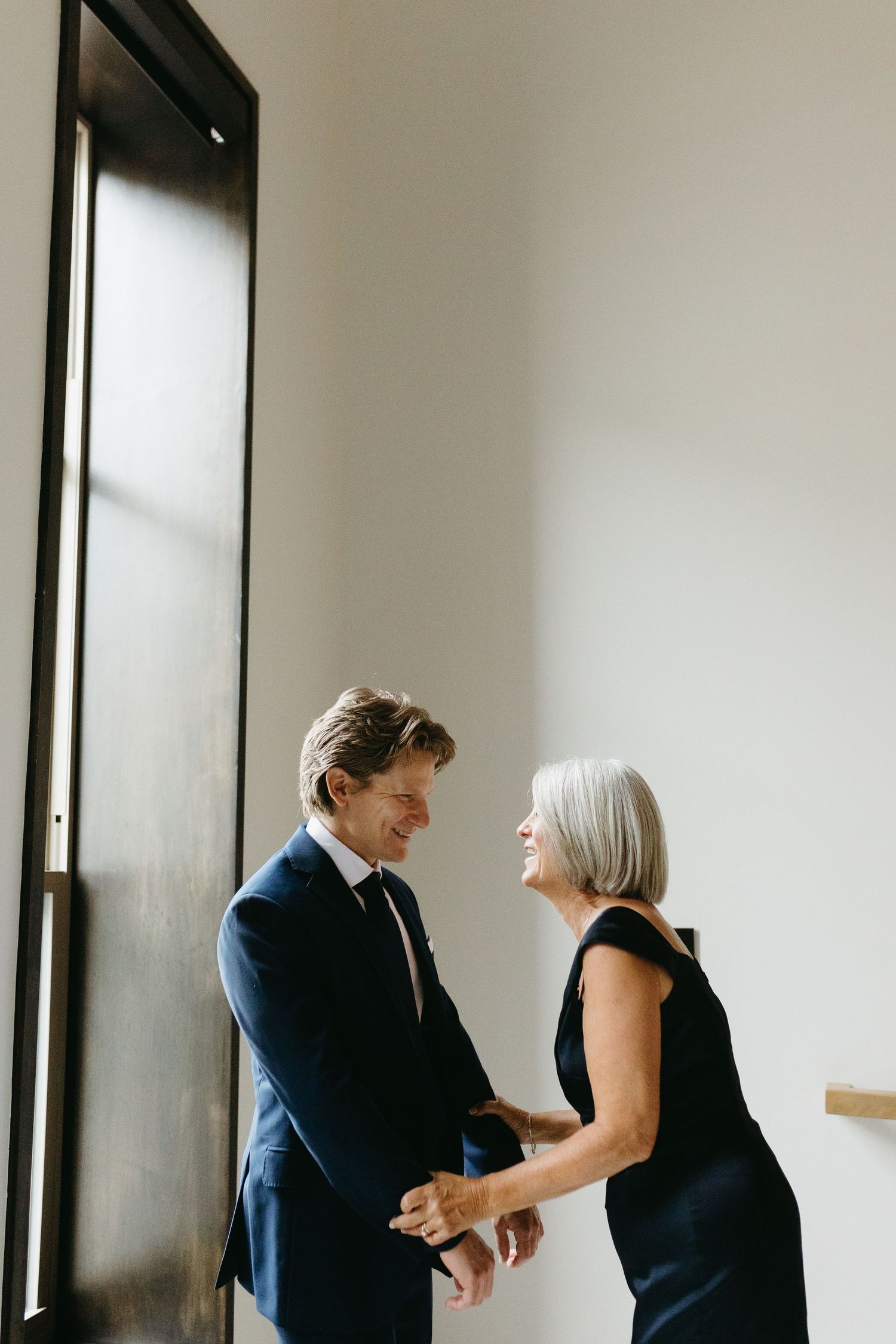 Professional couple in formal business attire dancing together in a bright, minimalist interior space.