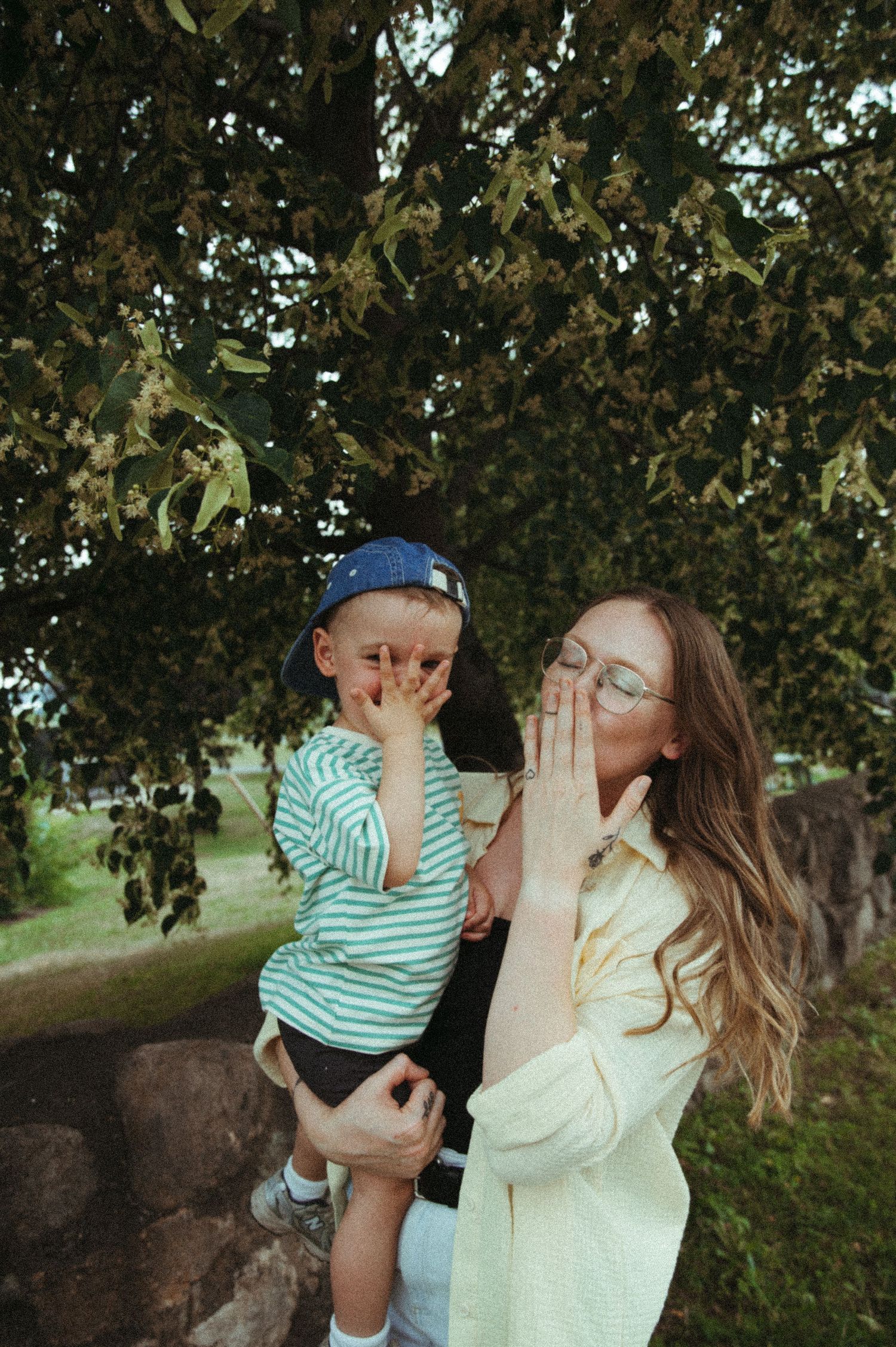 A playful outdoor moment between parent and child under autumn trees with sunlight filtering through.