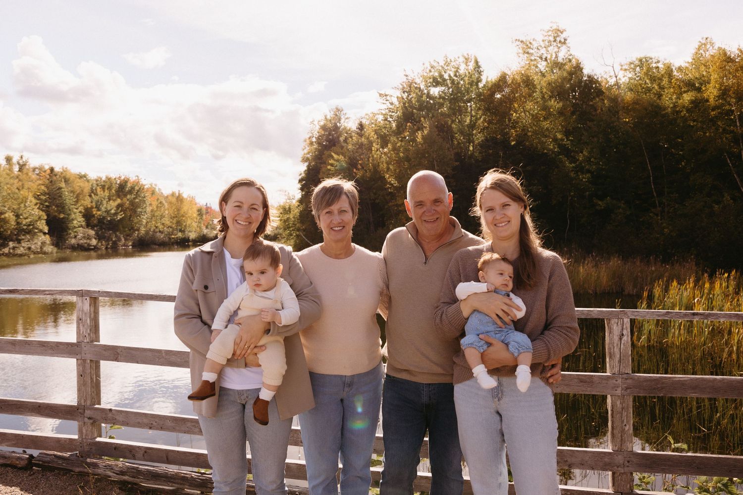 Multi-generational family group poses together on a wooden boardwalk near a lake during sunset.