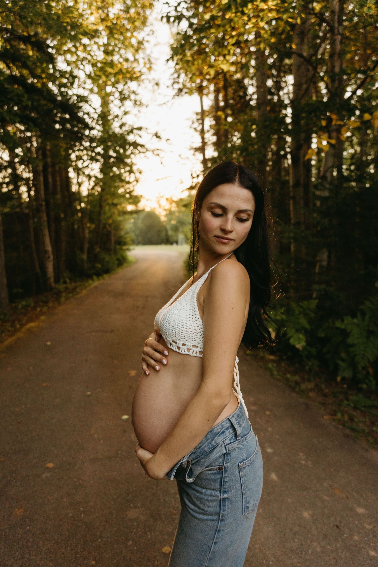 A dreamy maternity photo sequence showing a pregnant woman in overalls on a sunlit forest path at golden hour.