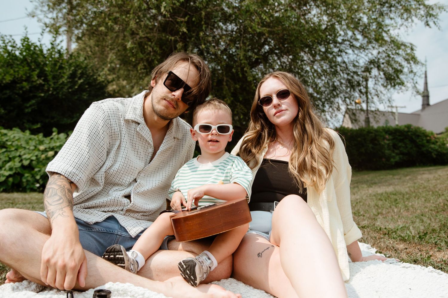 Group enjoying a sunny day outdoors on a blanket with sunglasses and casual attire.