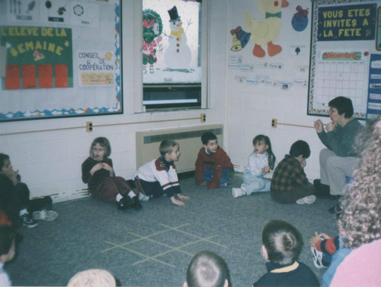 Students sit on the floor in a classroom decorated with colorful posters and educational materials on the walls.
