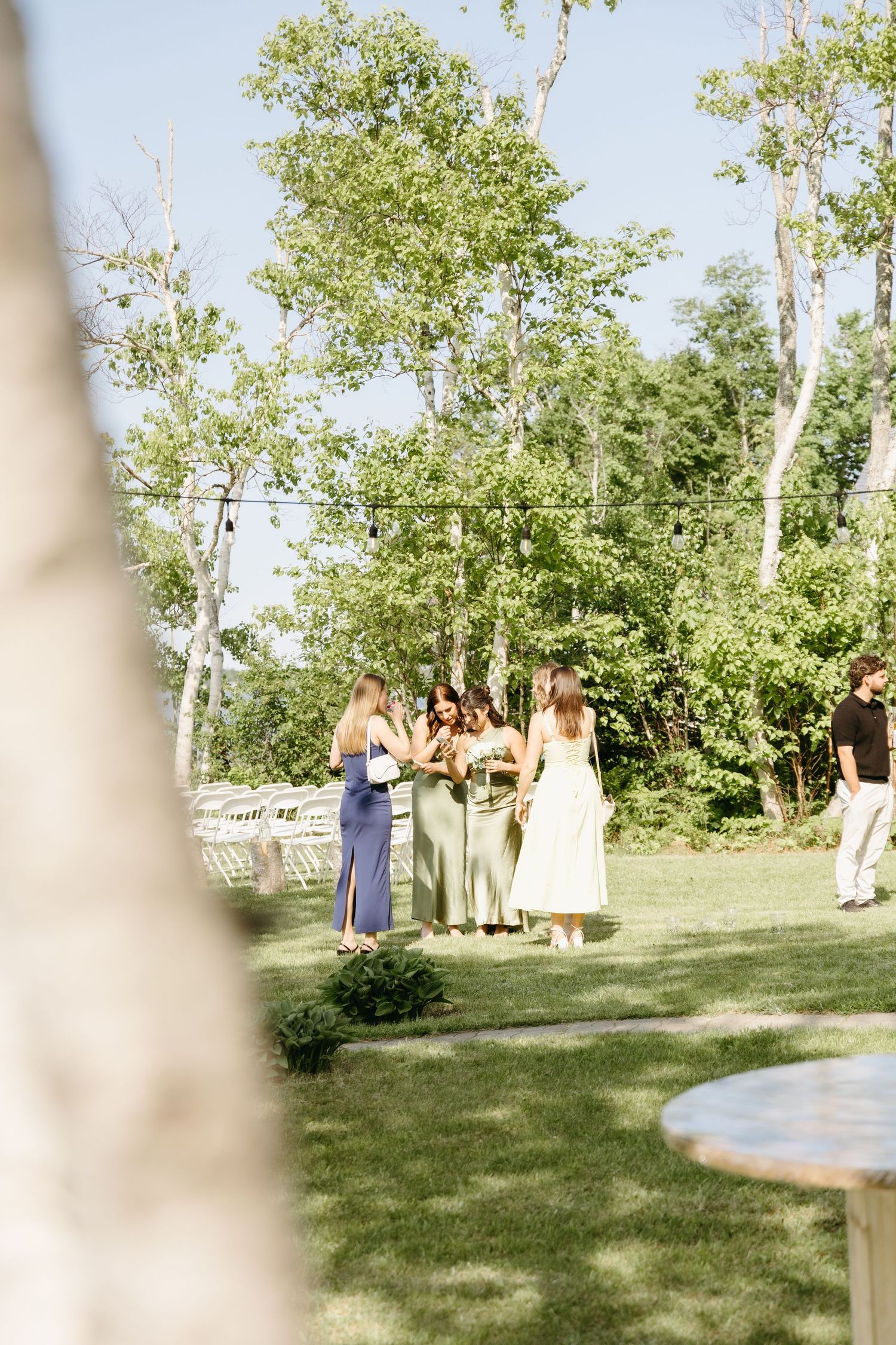 Outdoor wedding ceremony setup in a garden with white chairs and decorative columns on a sunny summer day.