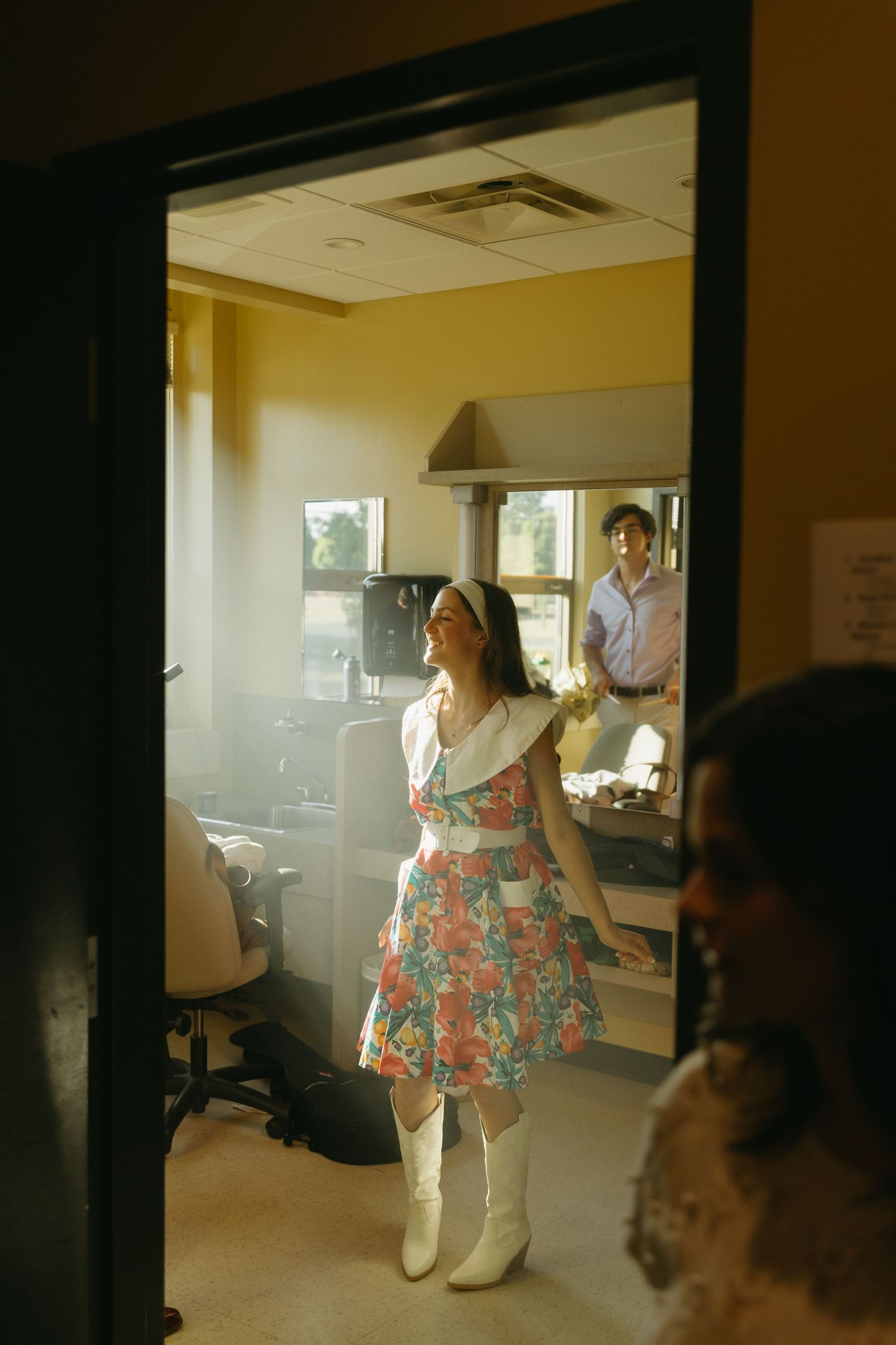A person in a floral print top stands in a bright office space with sunlight streaming through the windows.