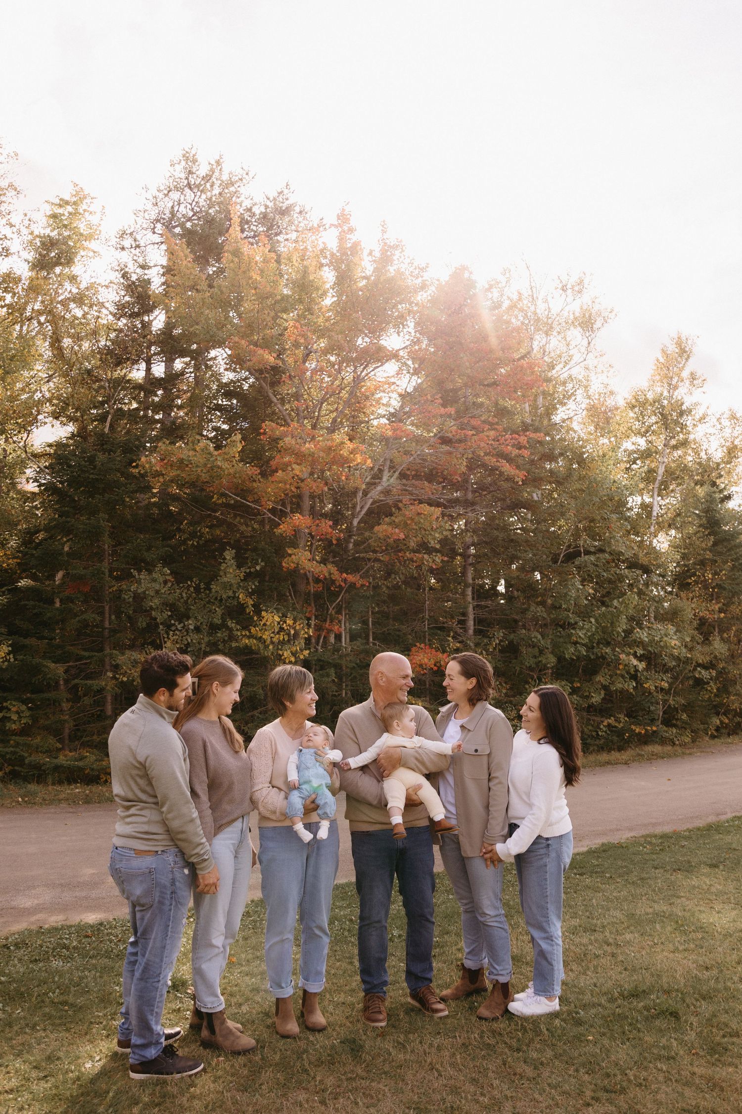Extended family gathers for group photos outdoors wearing coordinated neutral outfits on an autumn day.
