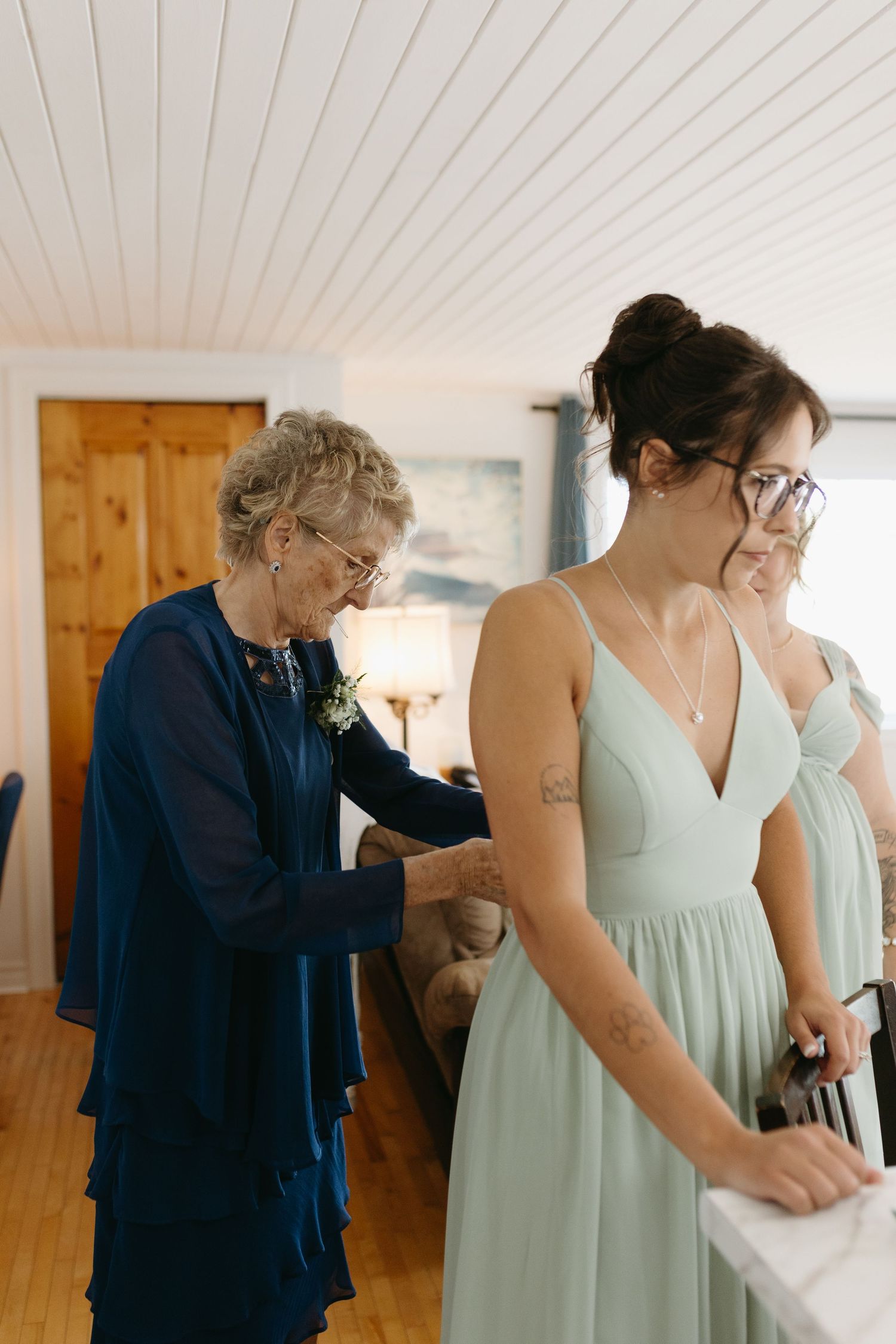 A person in a navy shirt helps another in a mint green dress with final adjustments during a wedding preparation.