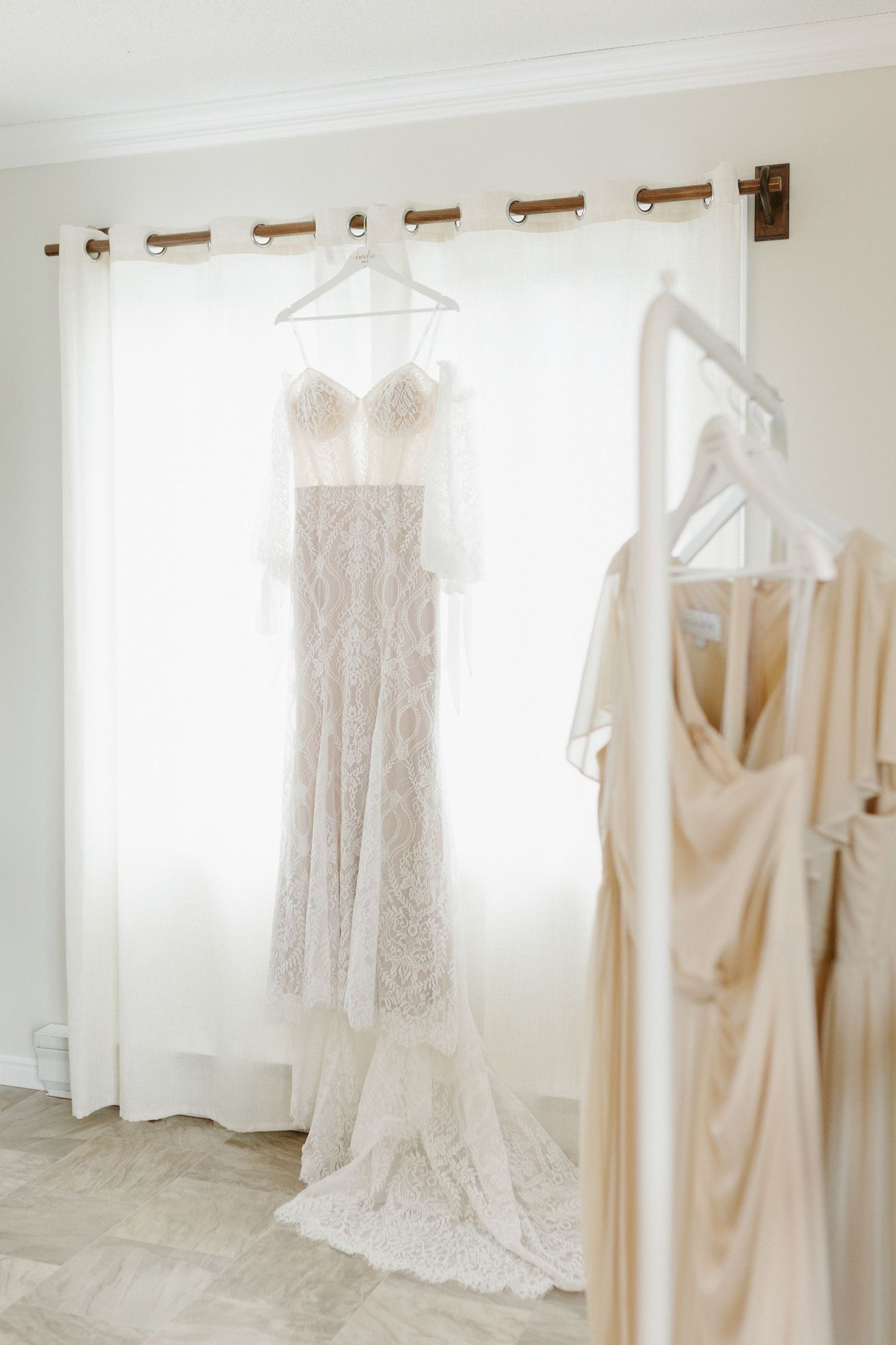 Multiple elegant white and ivory wedding dresses hanging on display in a bright, sunlit bridal boutique room.