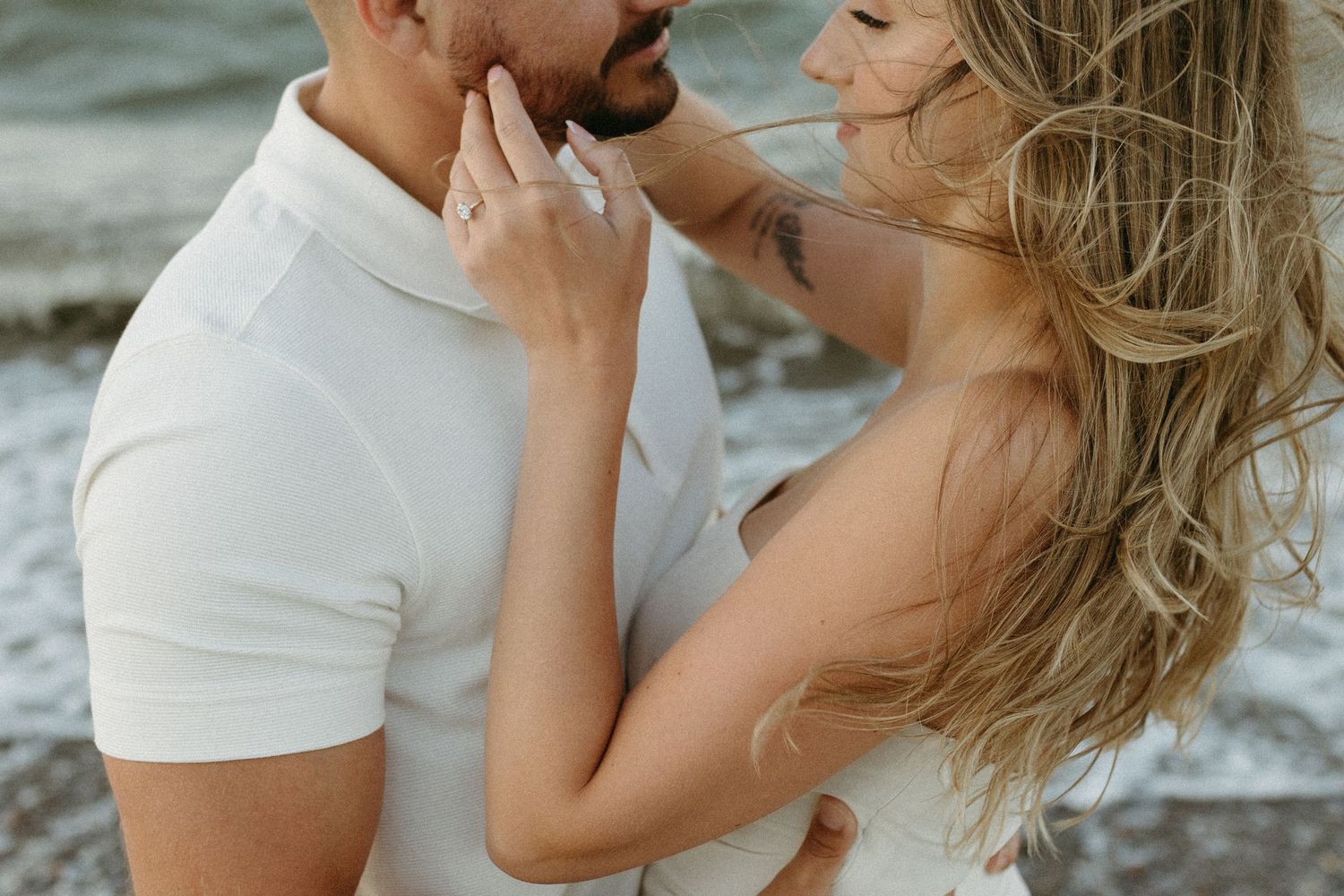 A romantic couple in white outfits shares an intimate moment by the ocean.