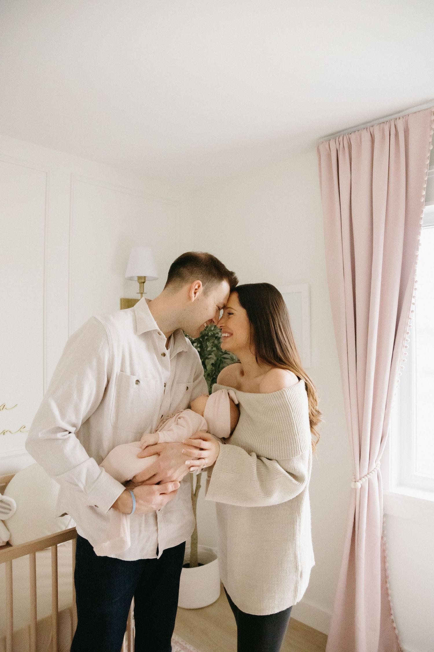 A couple in white shirts share tender moments in a bright room with pink curtains.