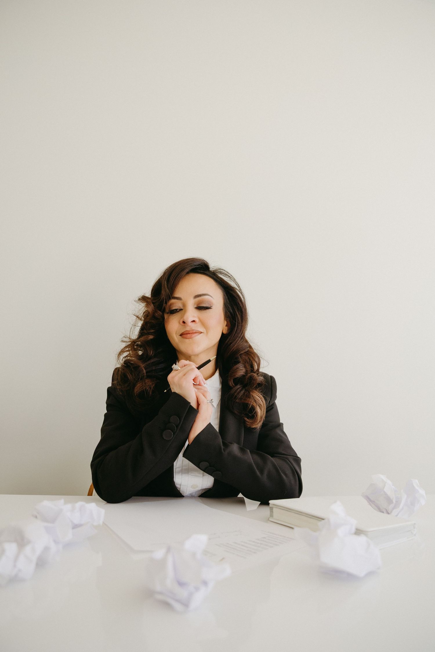 Professional wearing black blazer lies on white surface surrounded by crumpled paper showing different expressions.