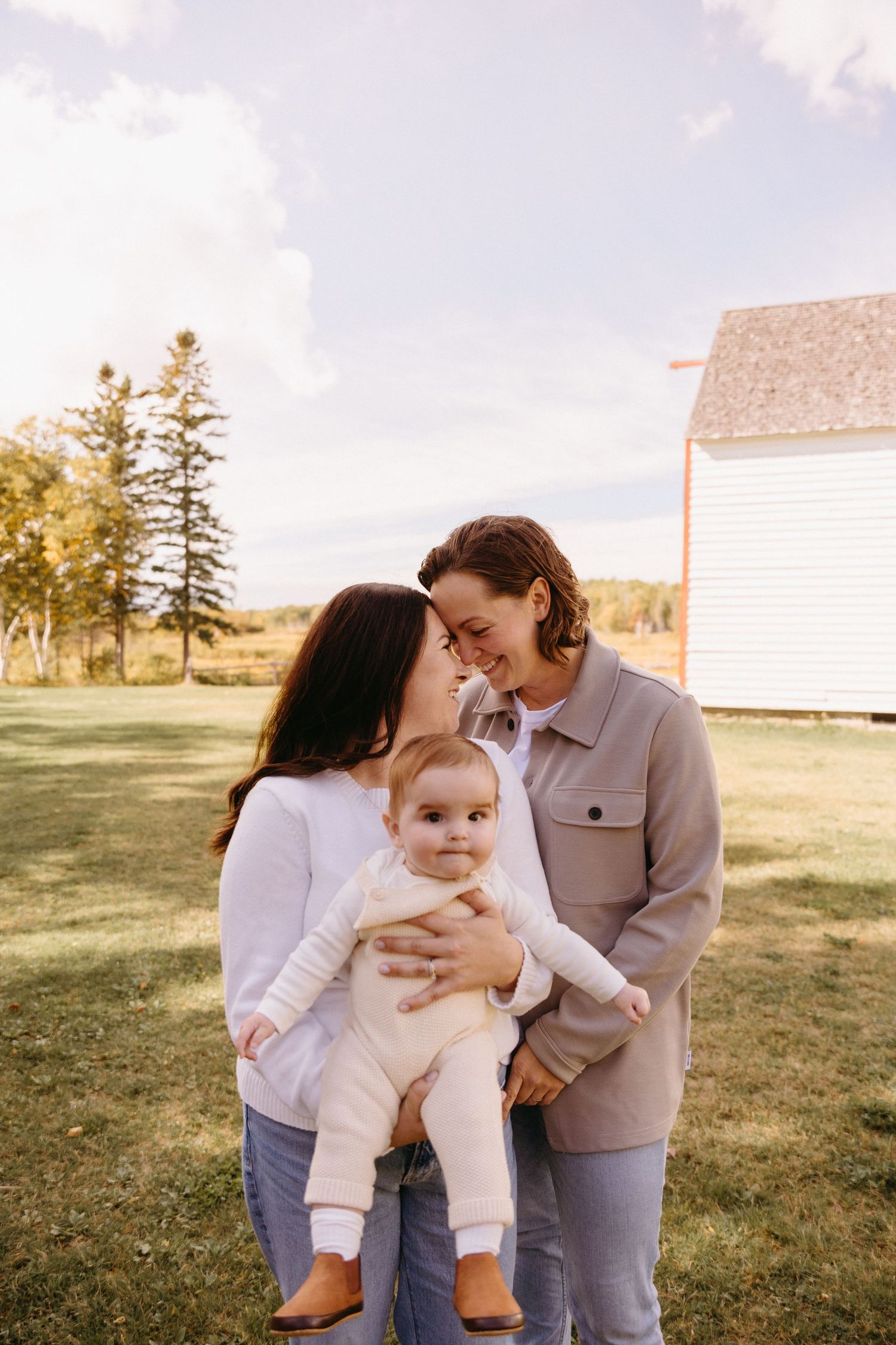 A couple shares tender moments with their baby outdoors in a grassy field during a warm autumn day.