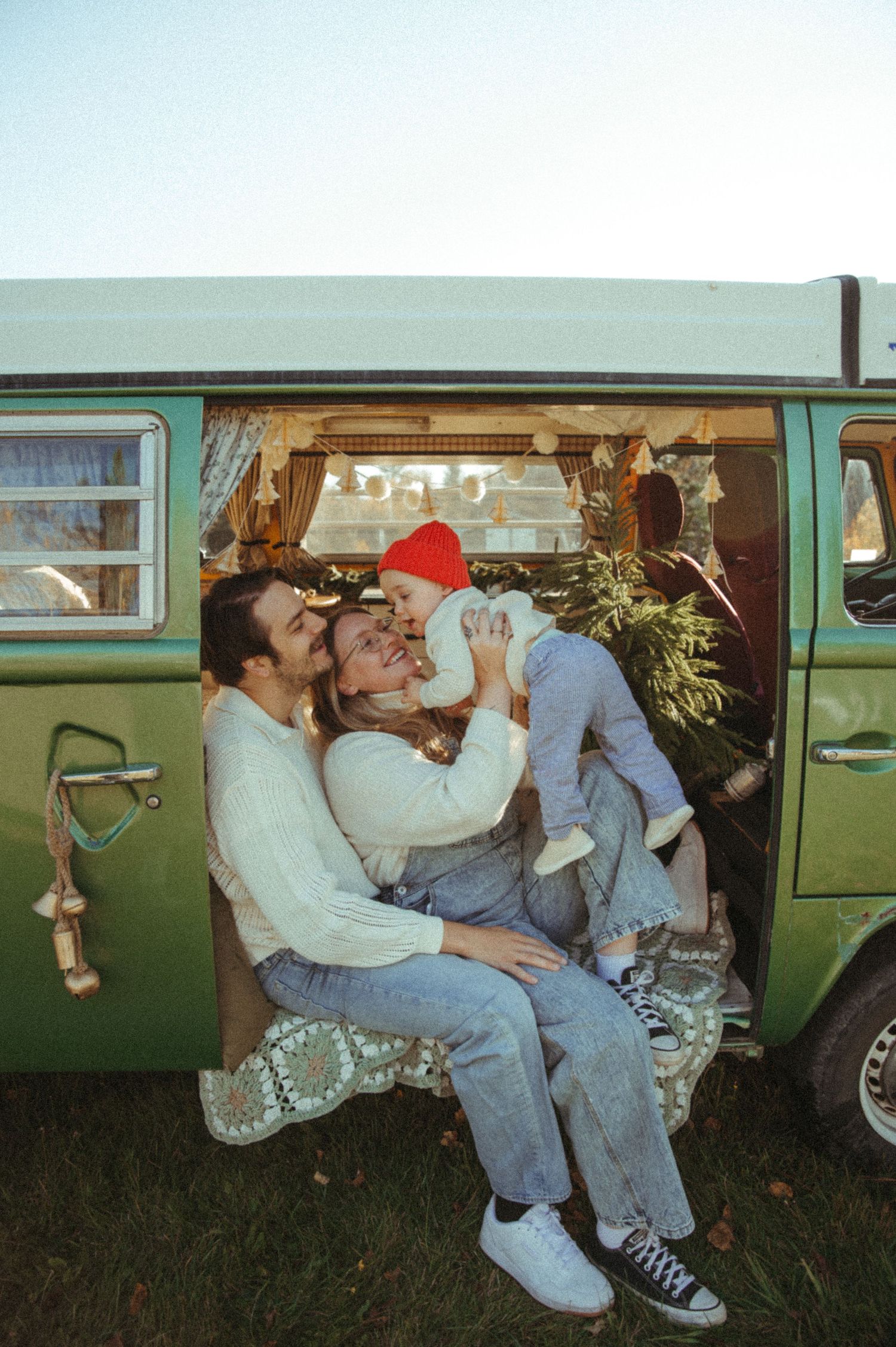Vintage green car parked on grass with people lounging and drinking beverages through the open windows.