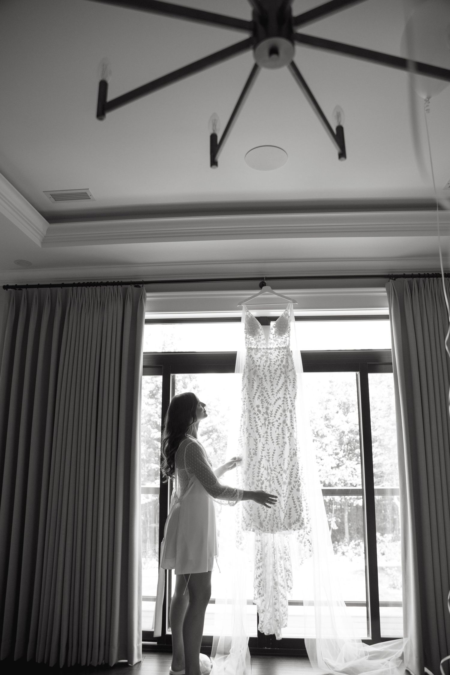 Silhouette of wedding dress hanging in window with figure standing nearby.
