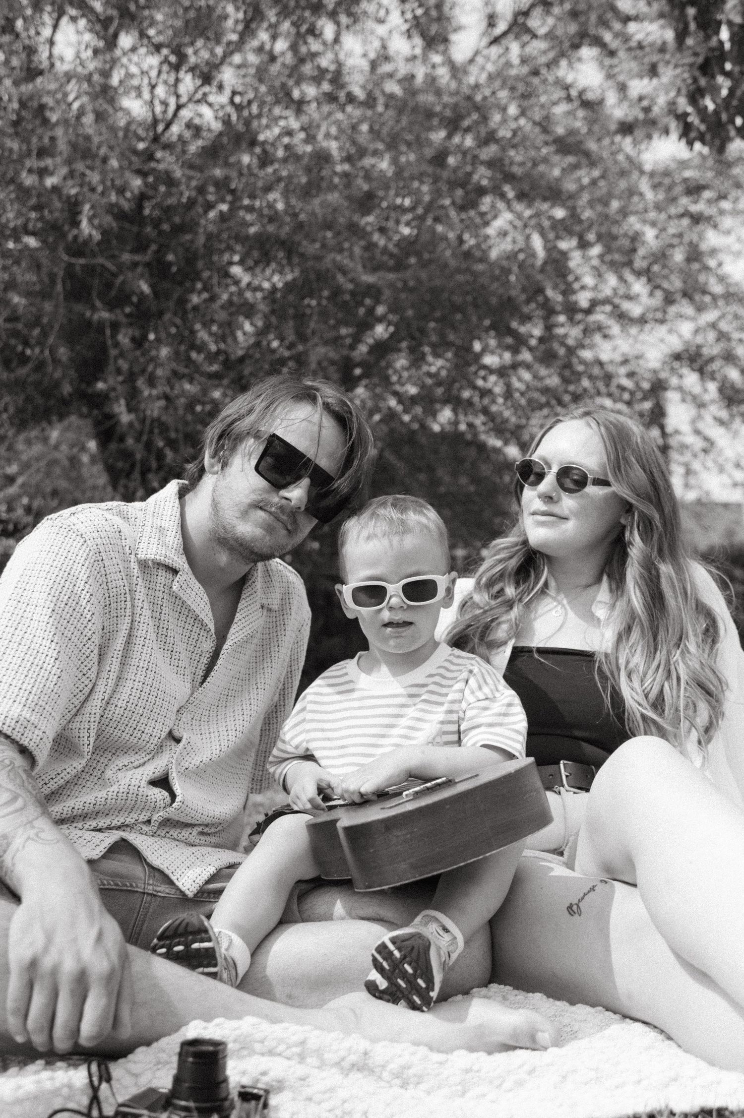 Black and white photo of a family enjoying a summer picnic outdoors, all wearing sunglasses while relaxing on a blanket.