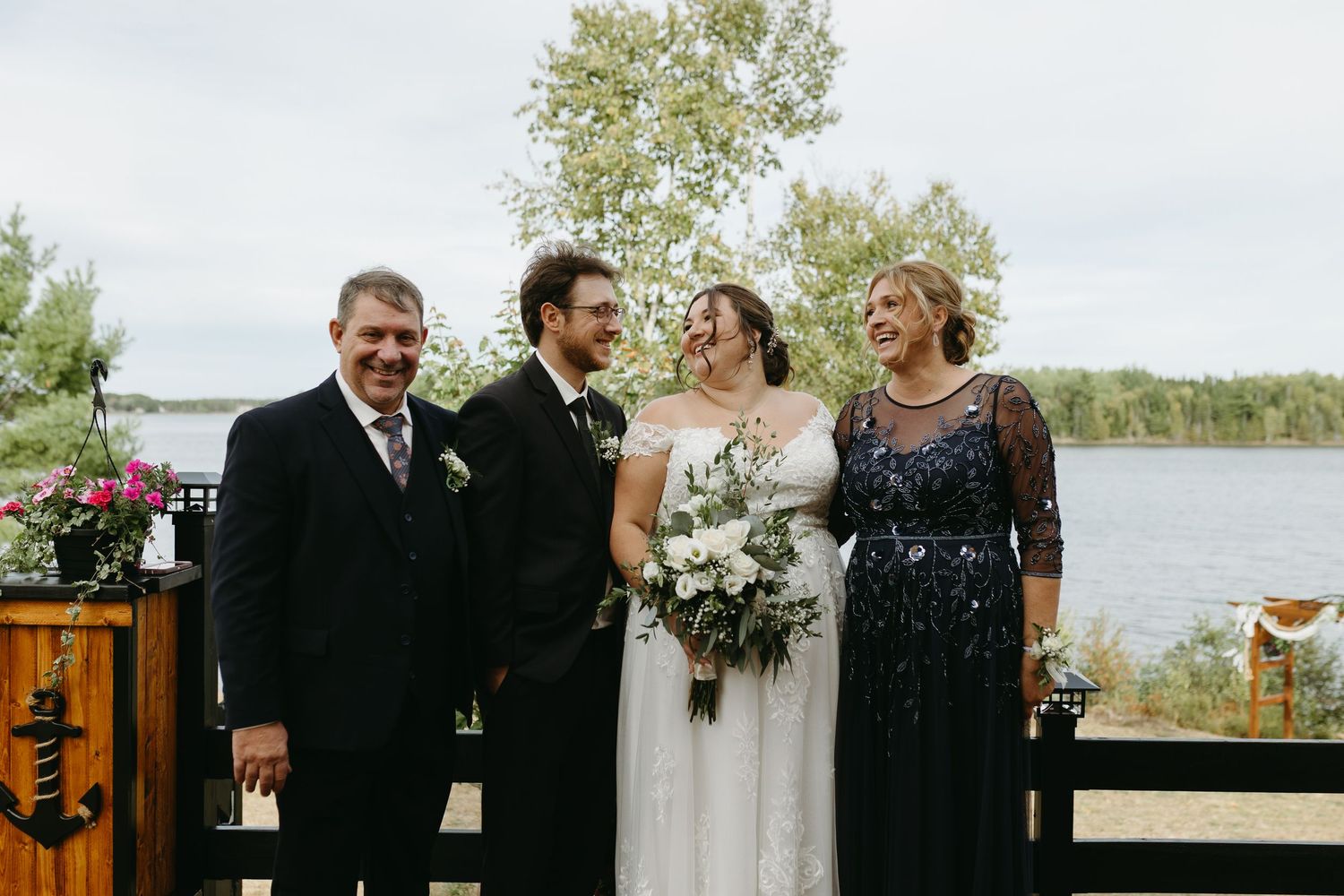 Wedding party members share joyful moments together outdoors by a waterfront on an autumn day.