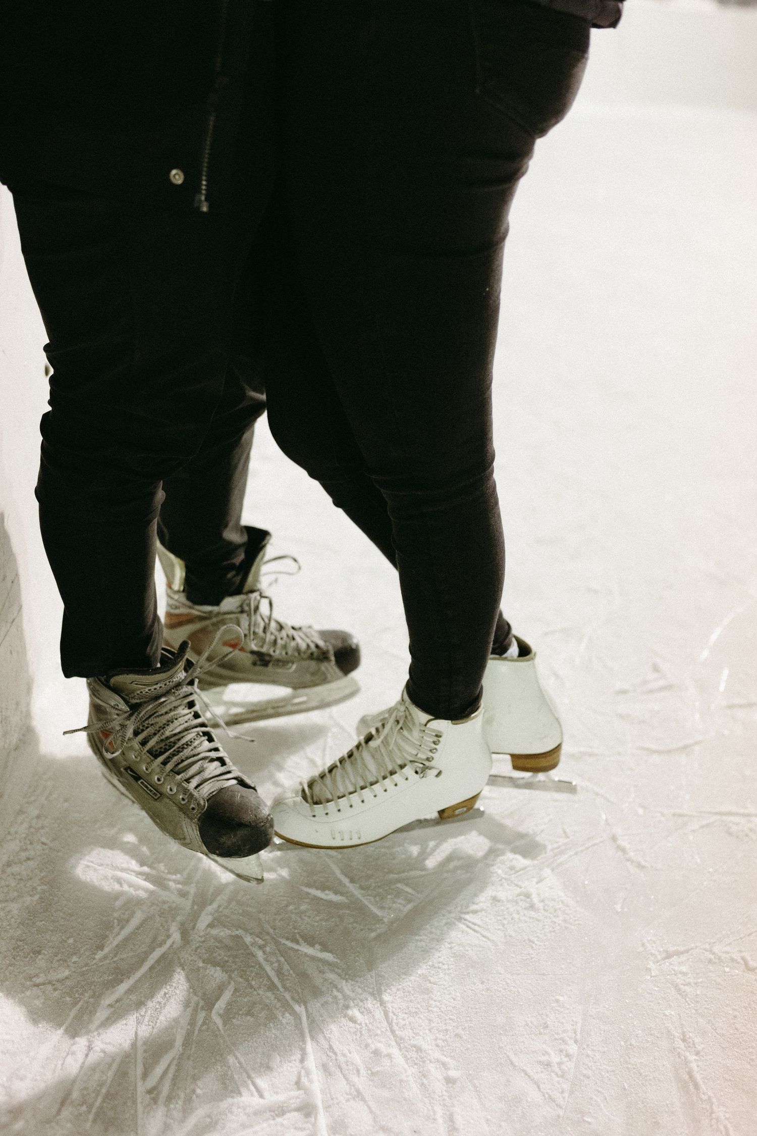 Close-up view of feet wearing white sneakers and black pants on a light-colored floor.