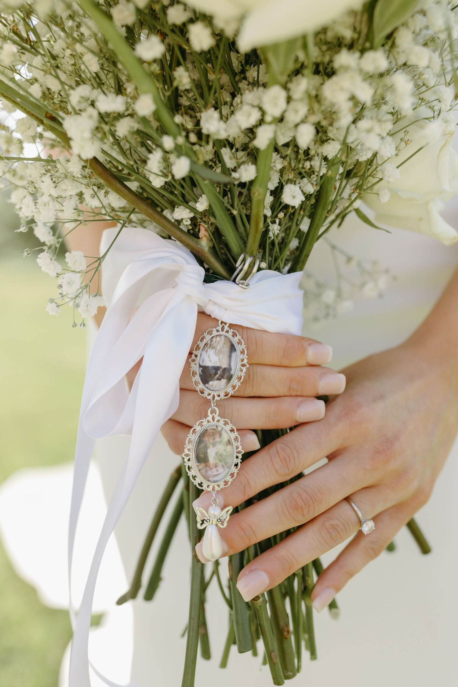 Close-up view of hands holding a delicate white bridal bouquet with baby's breath flowers and white ribbon details.