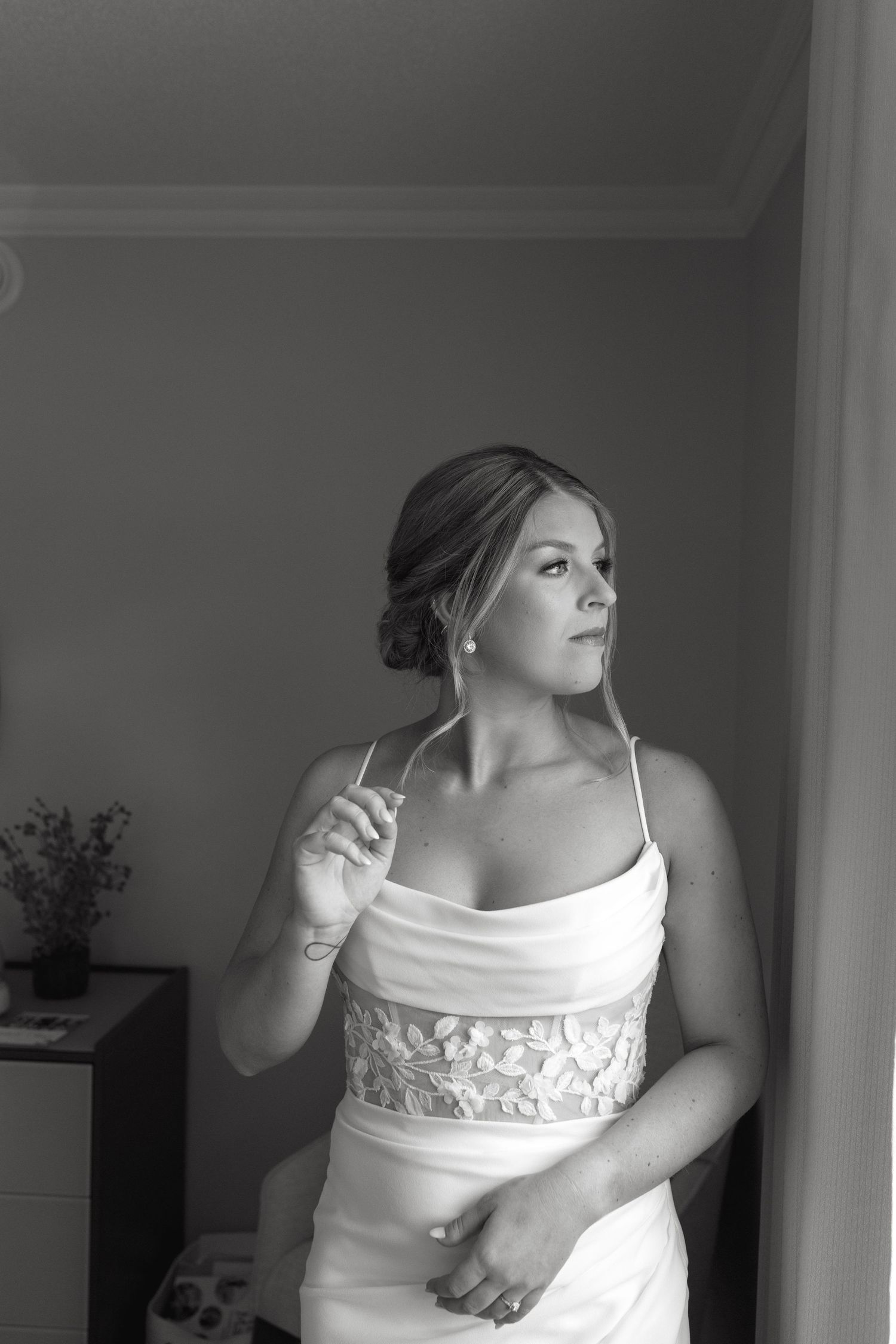 A black and white portrait of someone in a white wedding dress with lace details looking thoughtfully to the side.