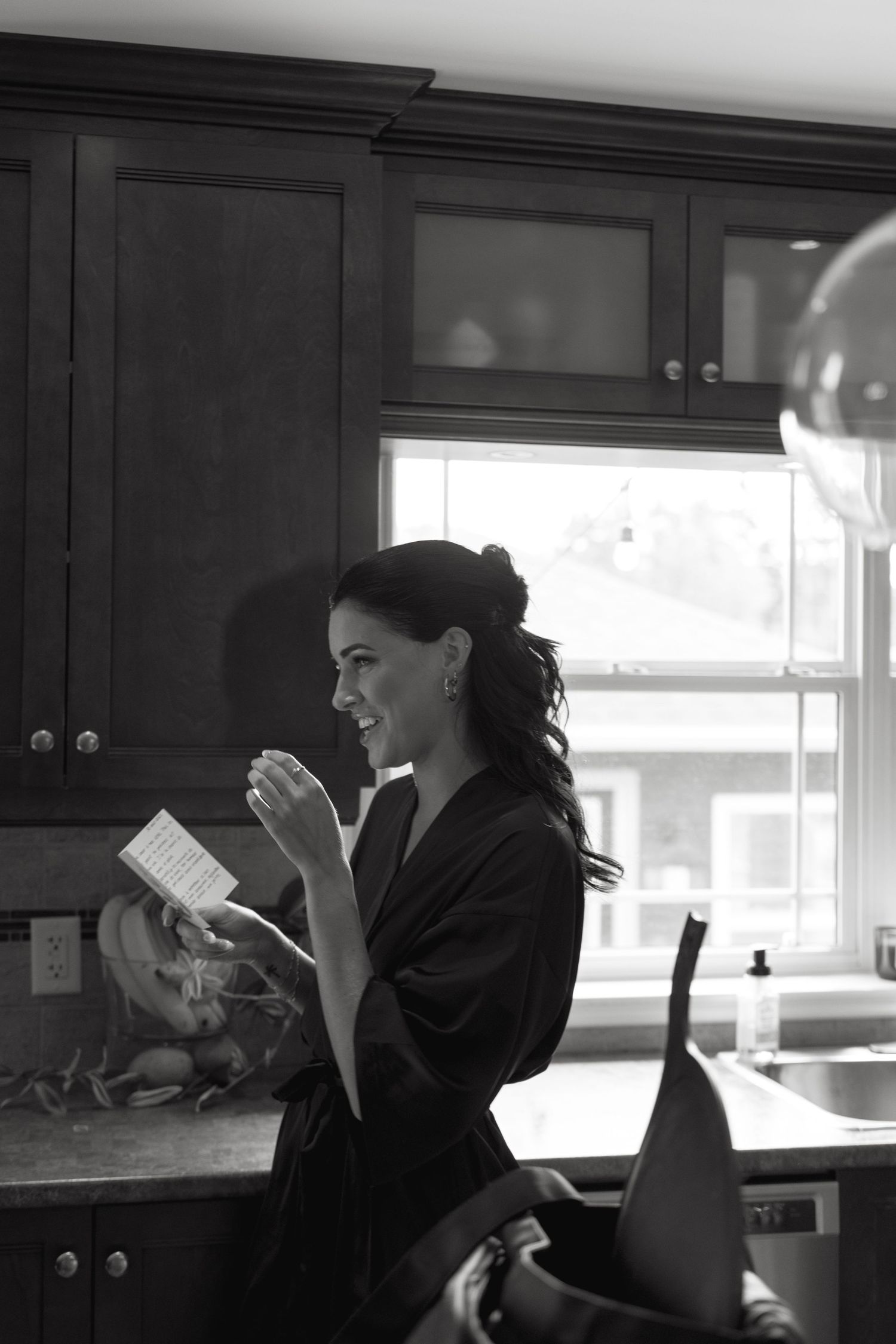 A sequence of black and white photos showing someone laughing while reading a book in a kitchen setting.