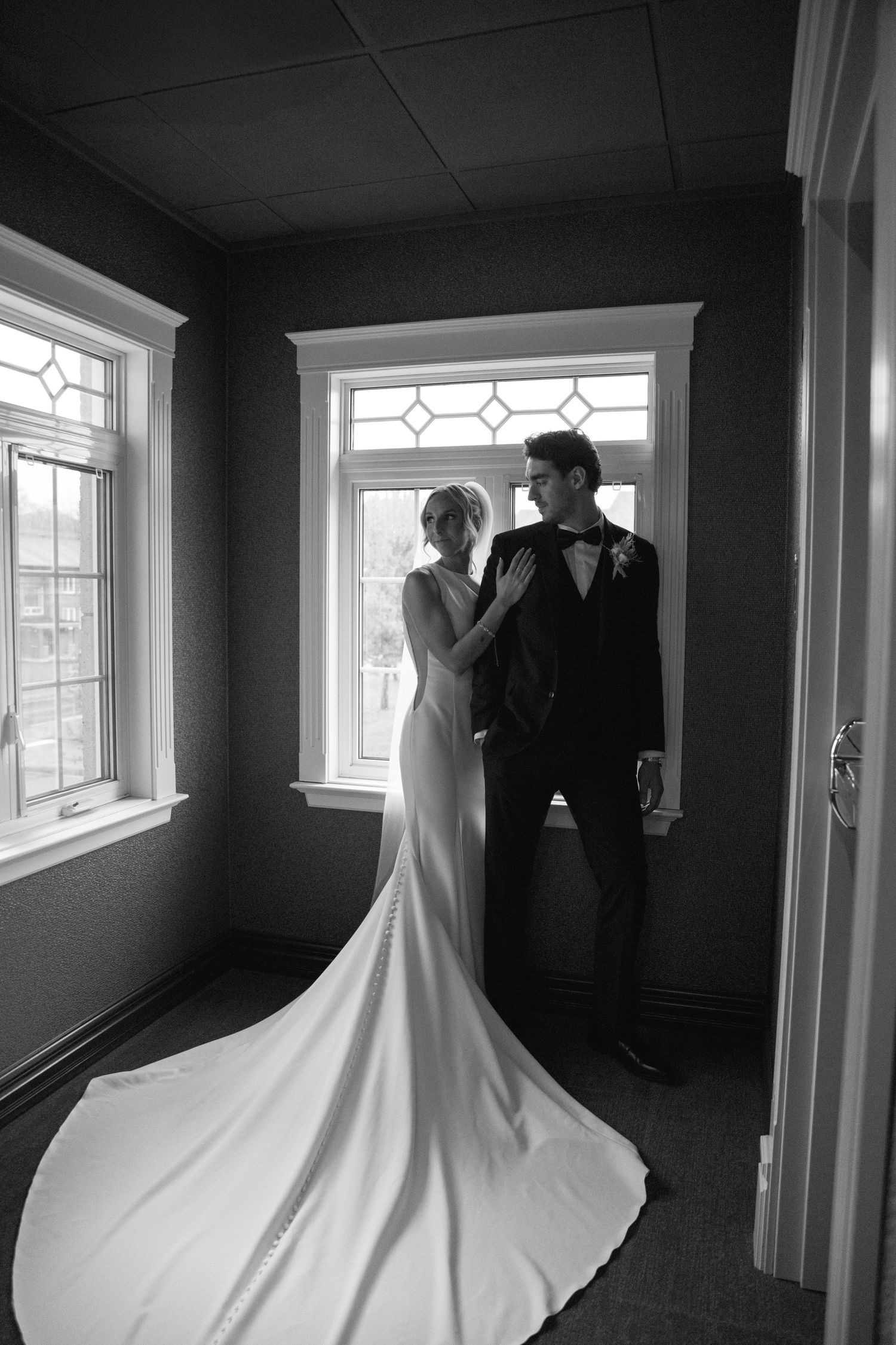 A black and white wedding photo series showing a couple in silhouette against bright windows in an elegant interior space.