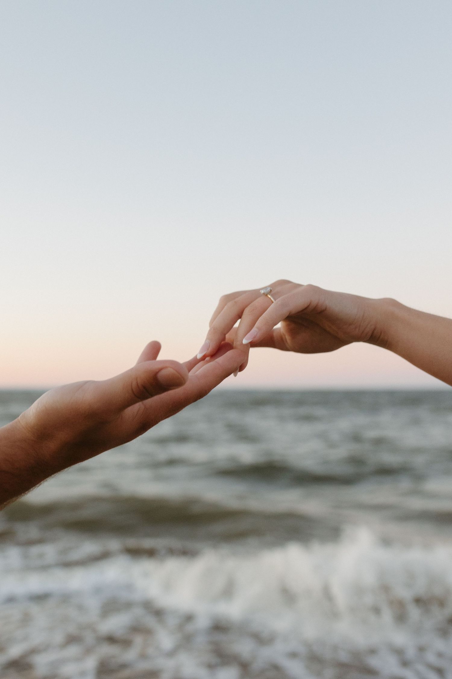 Two hands reaching towards each other against an ocean backdrop at sunset.